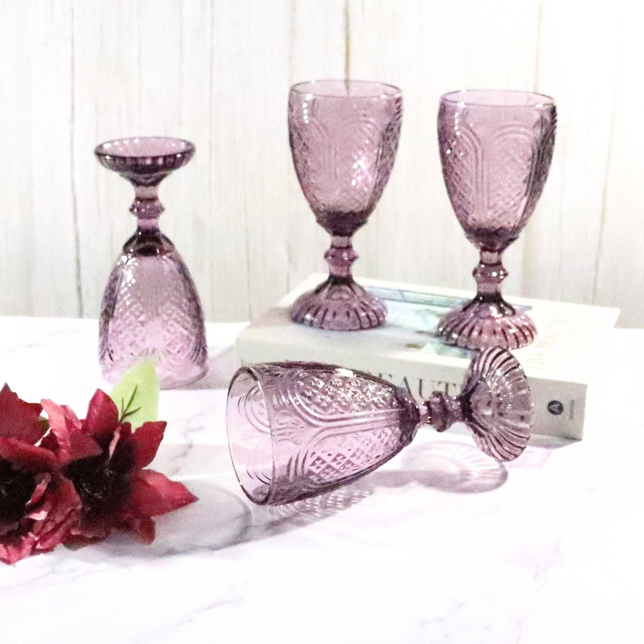 Set of purple glass goblets on a white surface with flowers.