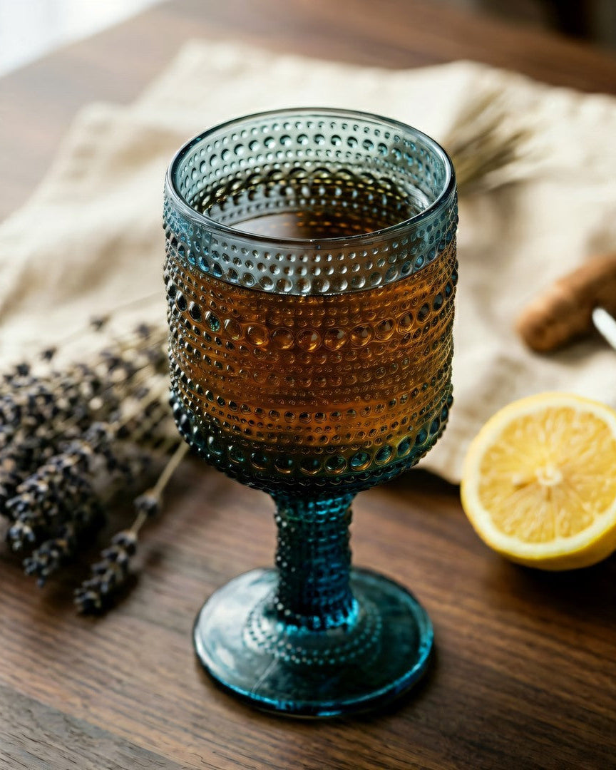 Blue textured glass with a drink on a wooden table with lemon and lavender.