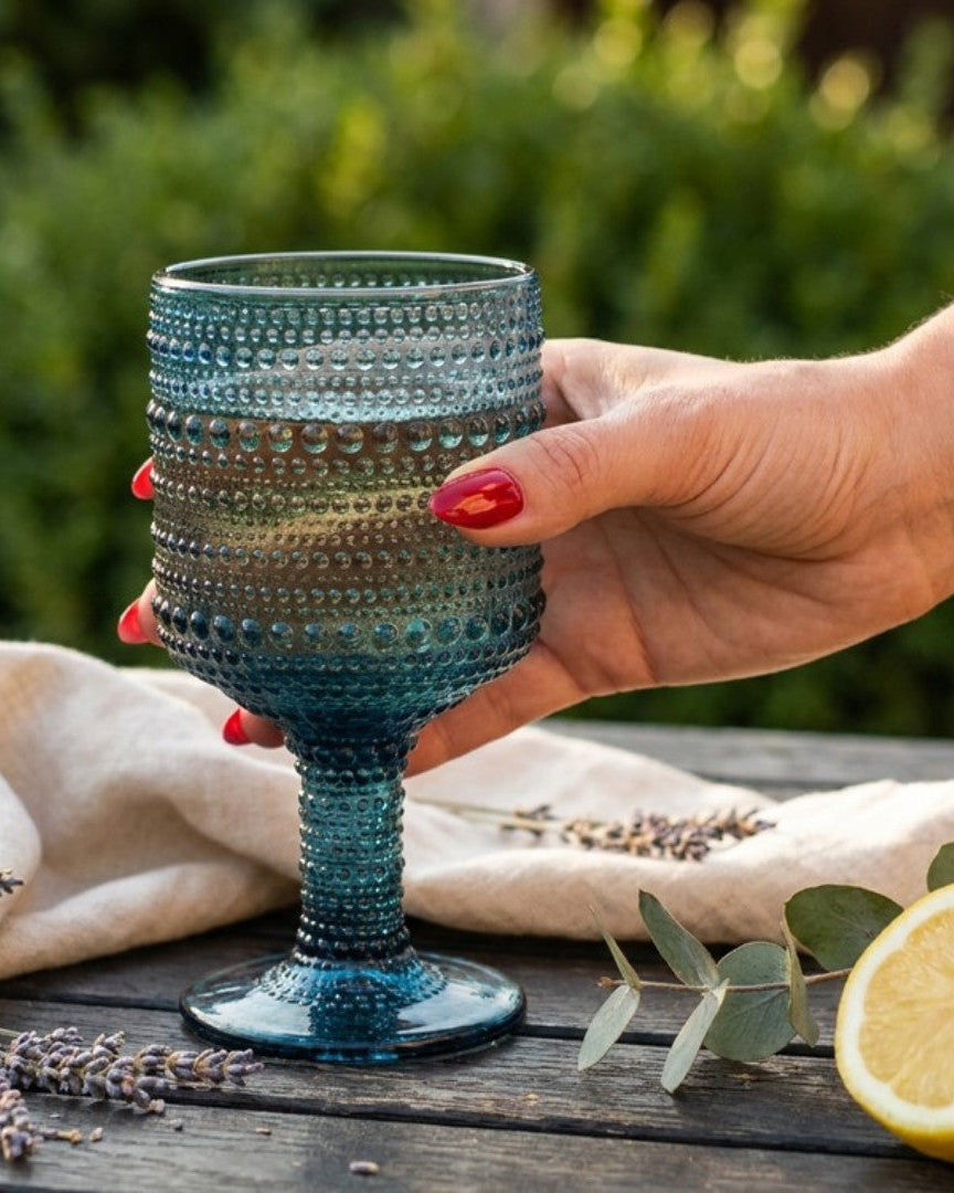 Hand holding a textured blue glass with lemons and lavender on a wooden surface