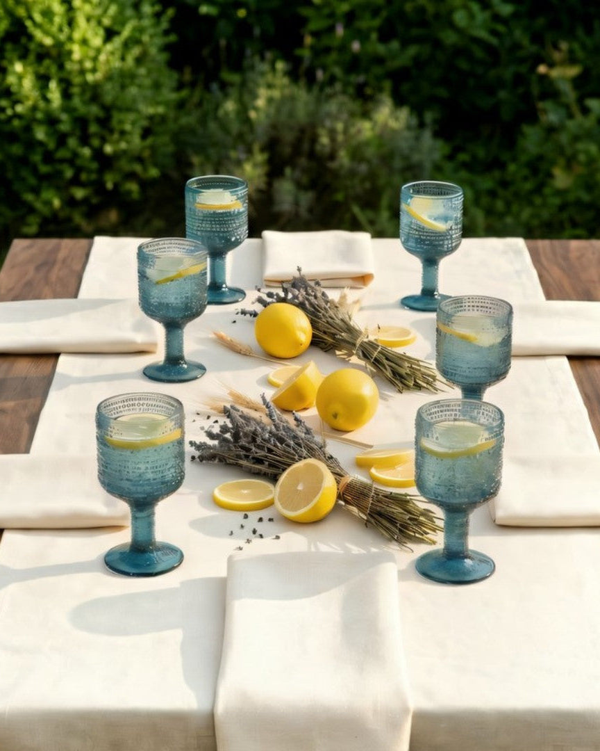Outdoor table setting with blue glasses, lemons, and lavender on a wooden table.