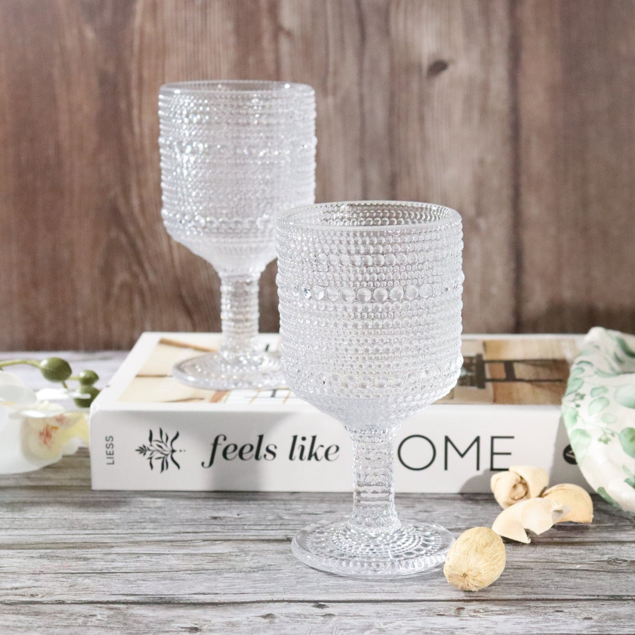 Two clear textured glass goblets on a wooden surface with a book underneath.