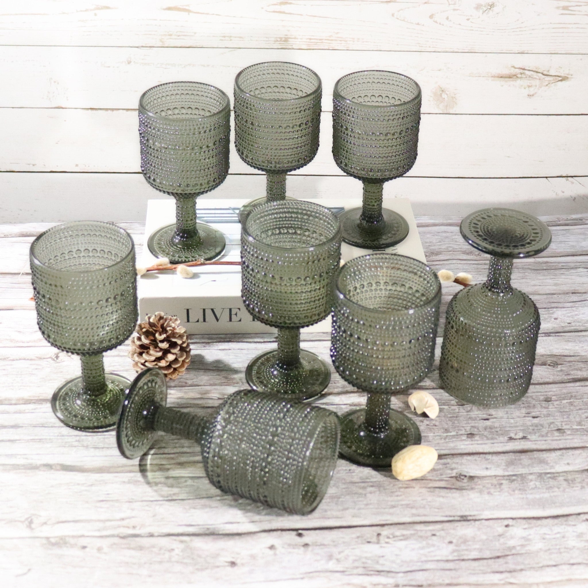Set of grey hobnail style textured glass goblets on a wooden surface with pine cones and books.
