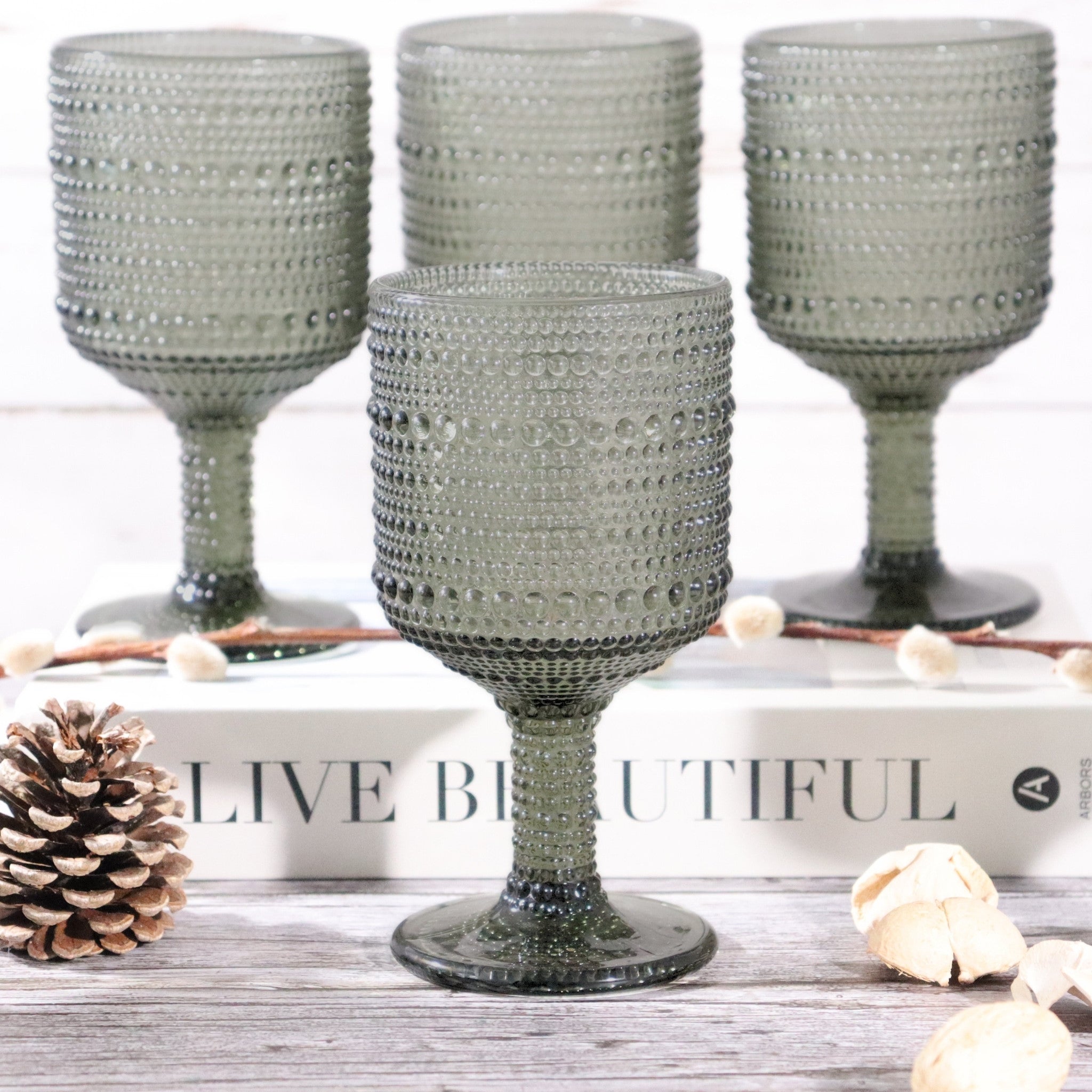 Set of four textured gray goblets on a decorative surface with 'Live Beautiful' sign.