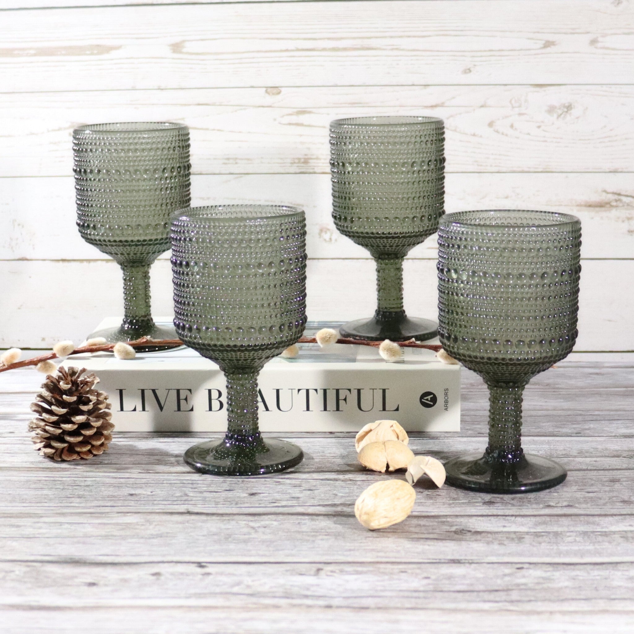 Set of four textured grey glass goblets on a wooden surface with decorative elements.