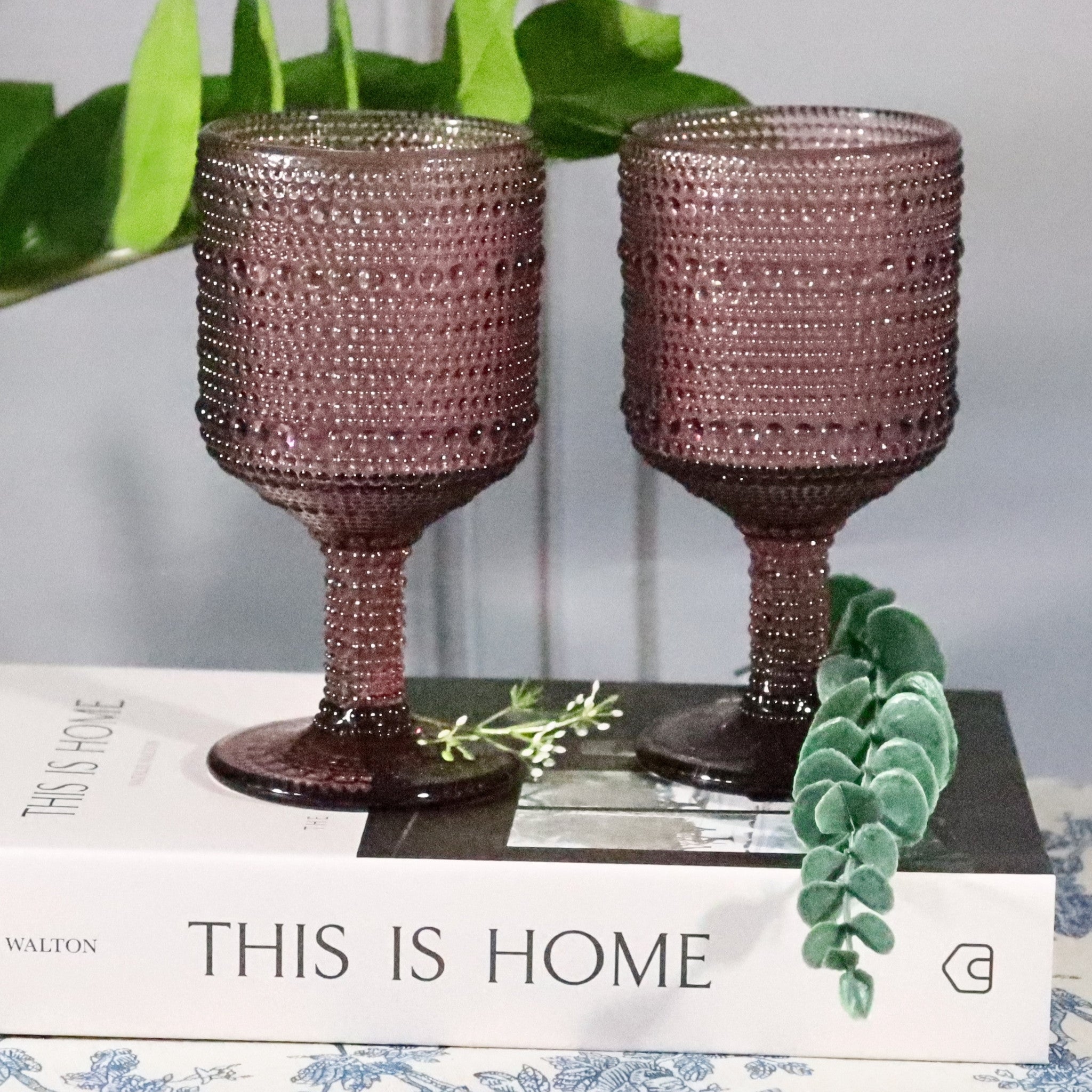 Two decorative purple goblets on a magazine with greenery in the background