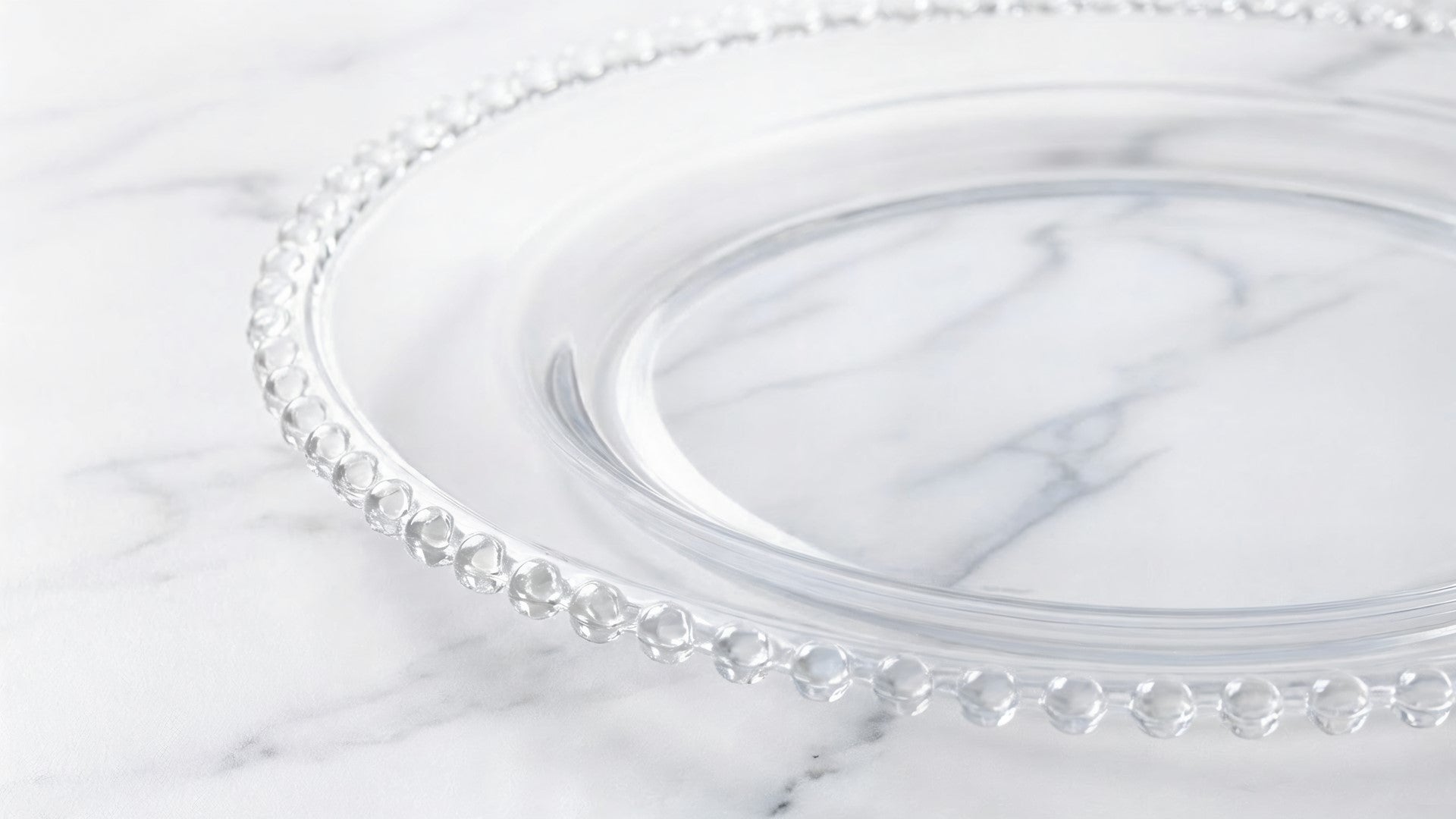 Clear glass plate with decorative rim on a marble surface