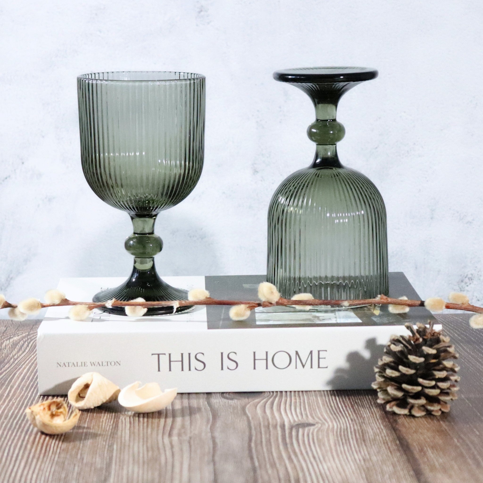 Two grey glass goblets on a book with decorative elements on a wooden surface.