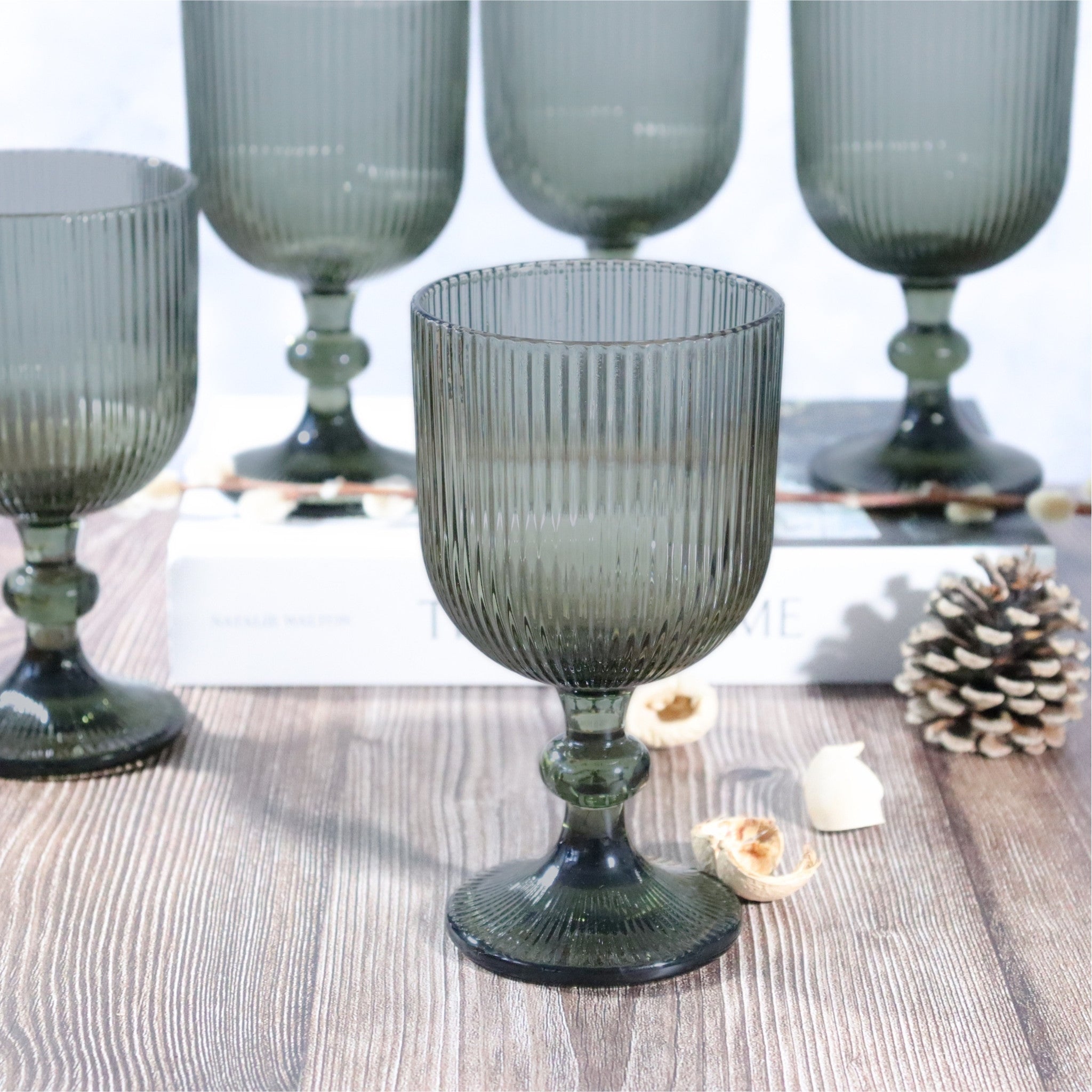 Set of ribbed glass goblets on a wooden surface with decorative elements.