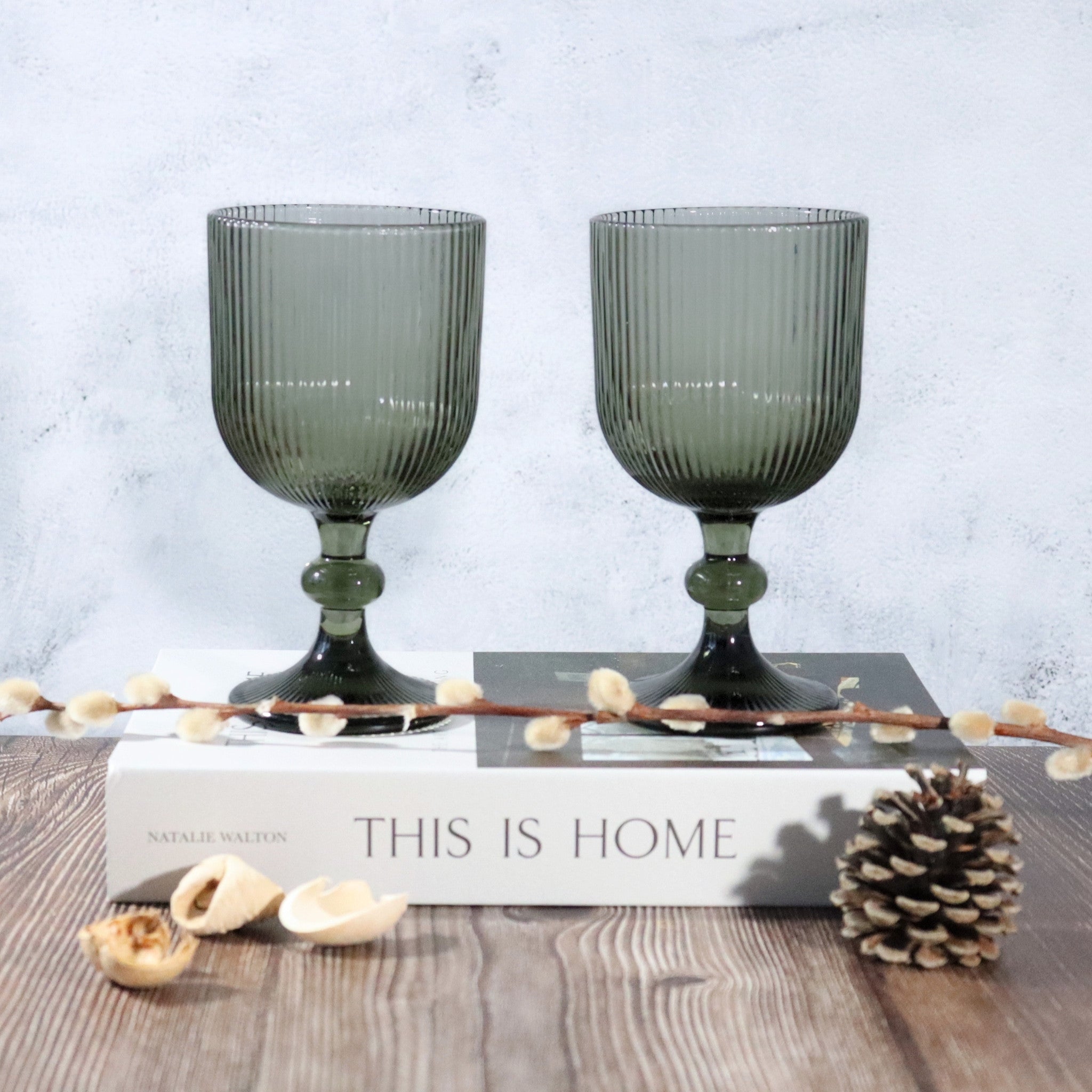 Two grey glass goblets on a book with decorative elements on a wooden surface.