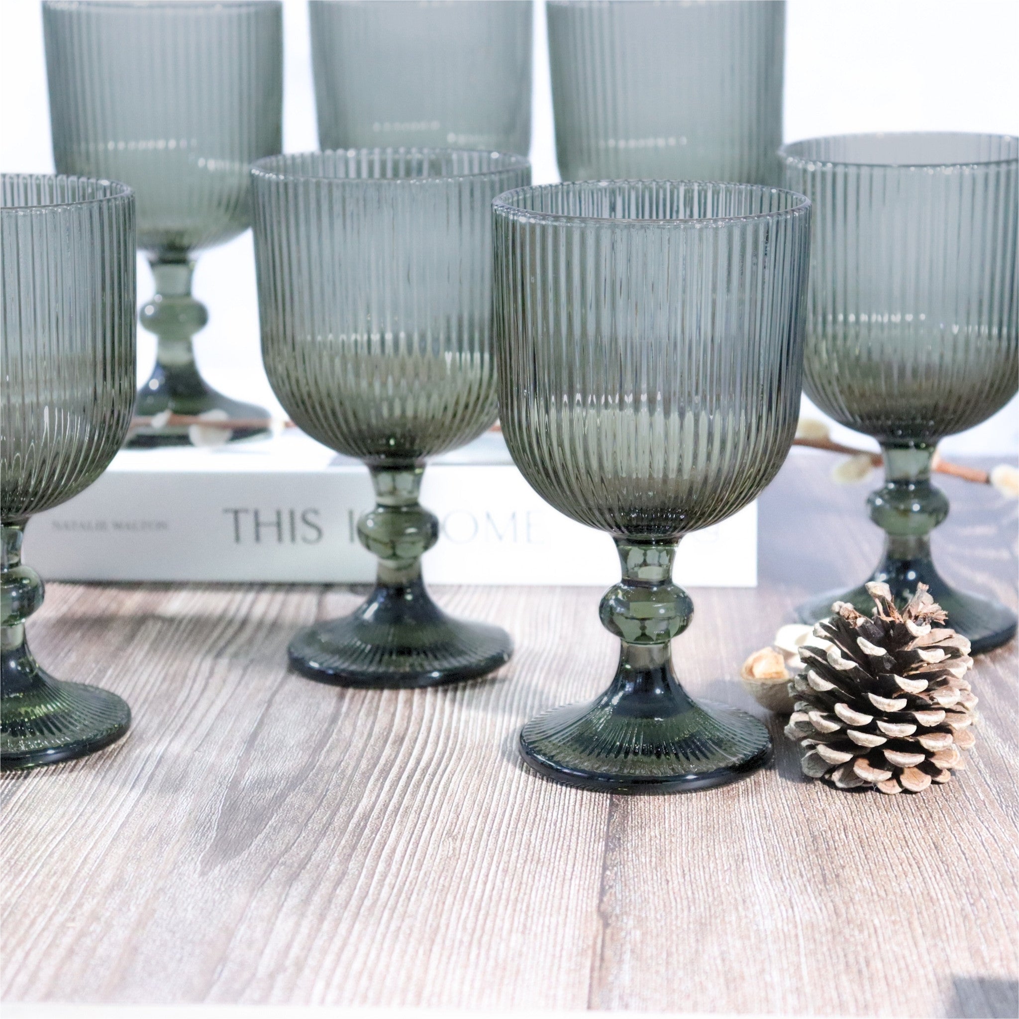 Set of ribbed glass goblets on a wooden surface with a pine cone.