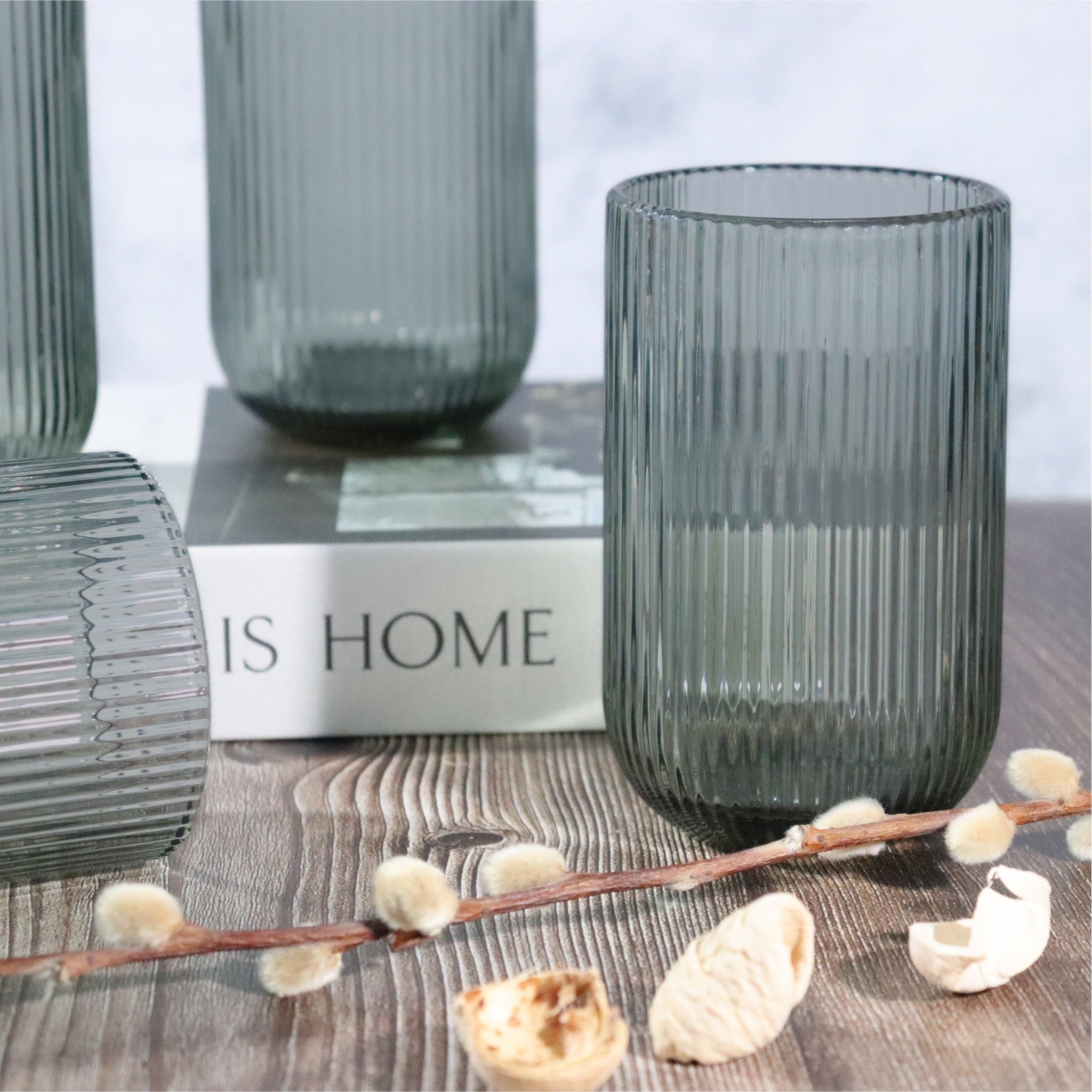 Set of ribbed glass vases on a wooden surface with 'IS HOME' sign in the background