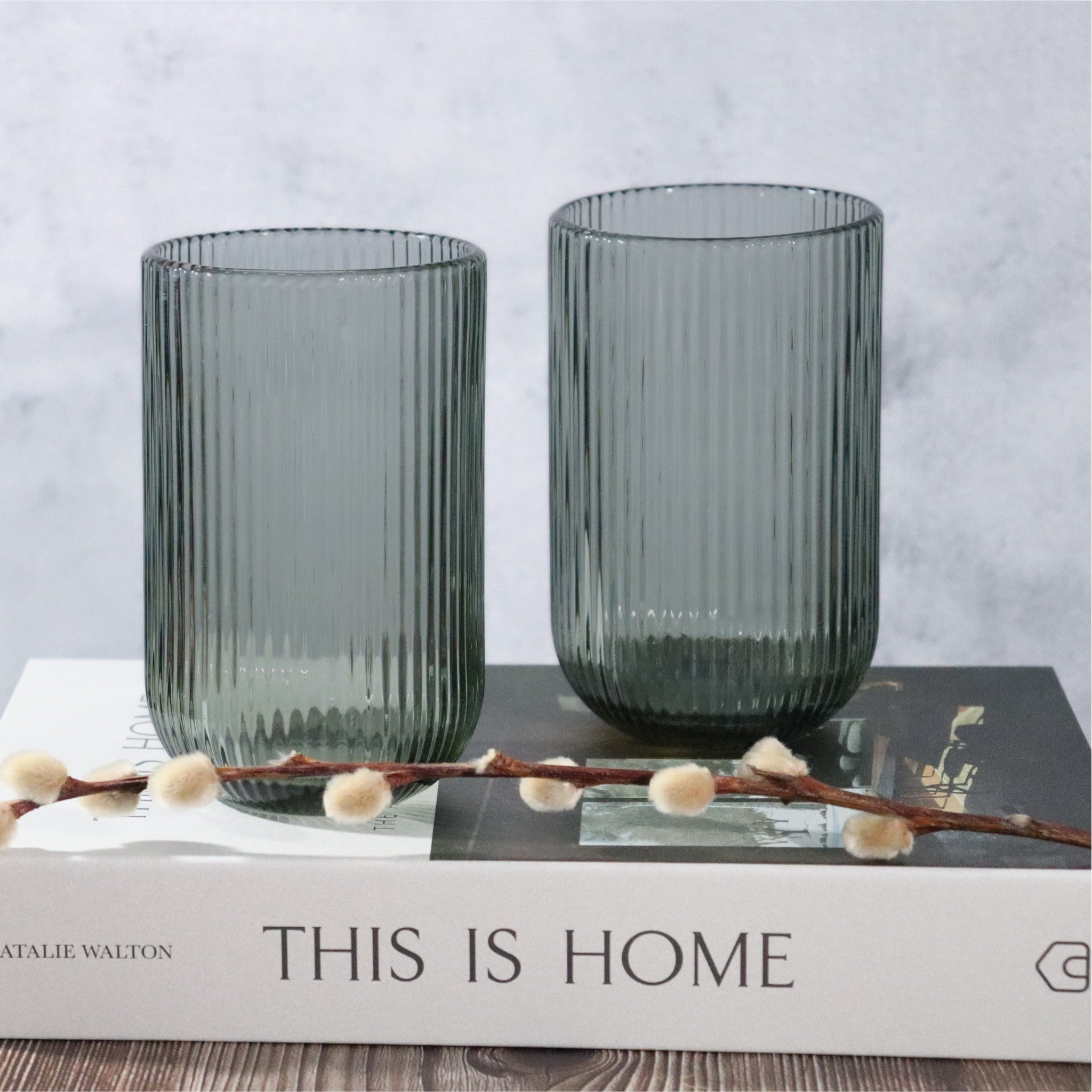 Two ribbed glass vases on a book with 'This is Home' text, against a light gray background.