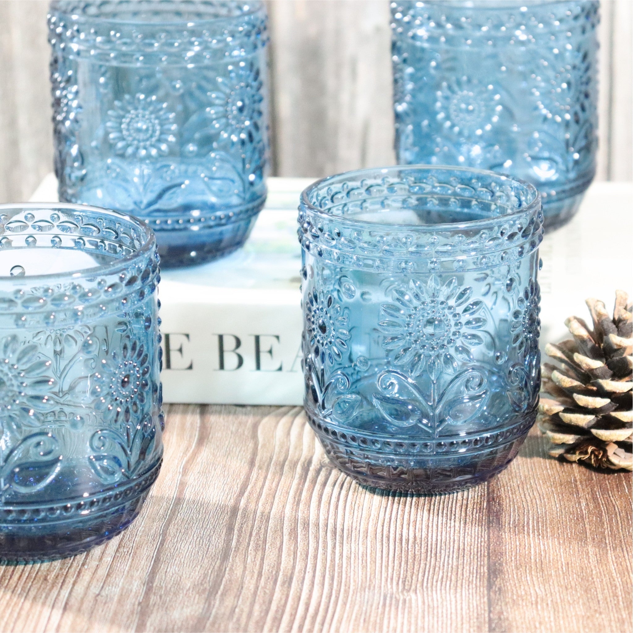 Set of blue glass tumblers with embossed designs on a wooden surface.