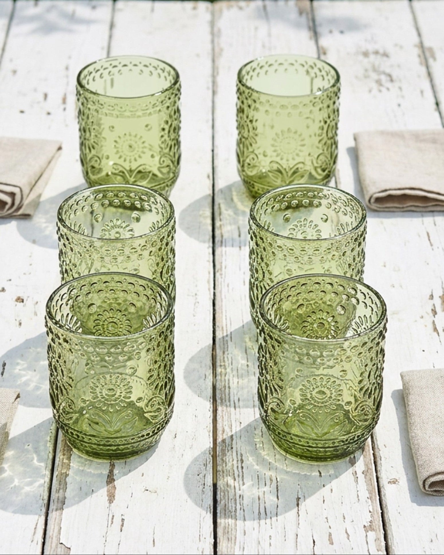 Set of green glass tumblers on a wooden table with beige napkins.