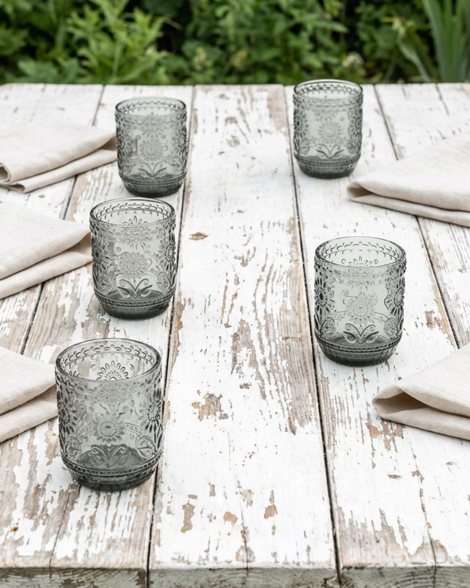 Set of six gray glass tumblers on a wooden table with beige napkins.