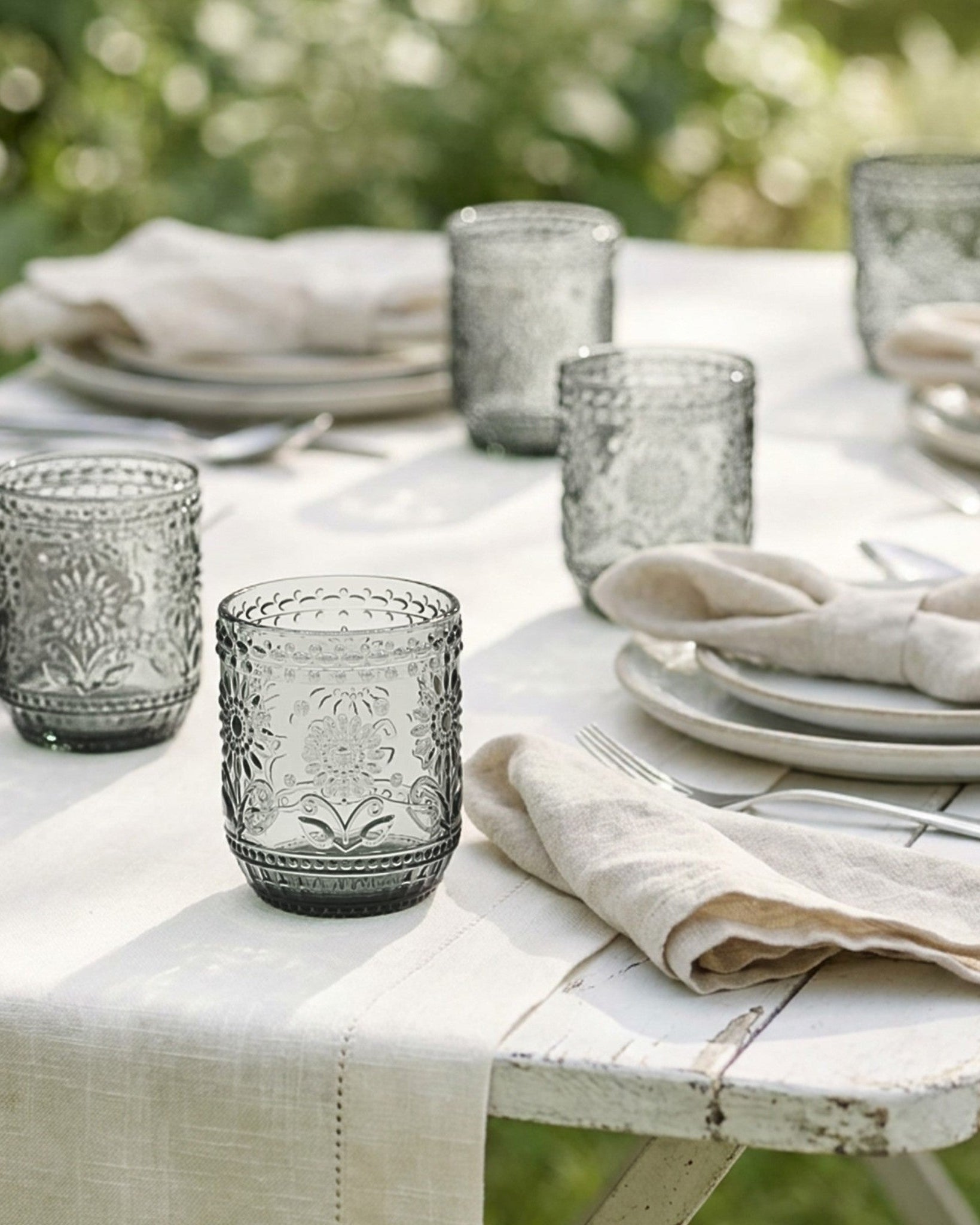 Outdoor table setting with gray glassware and white plates on a white tablecloth.