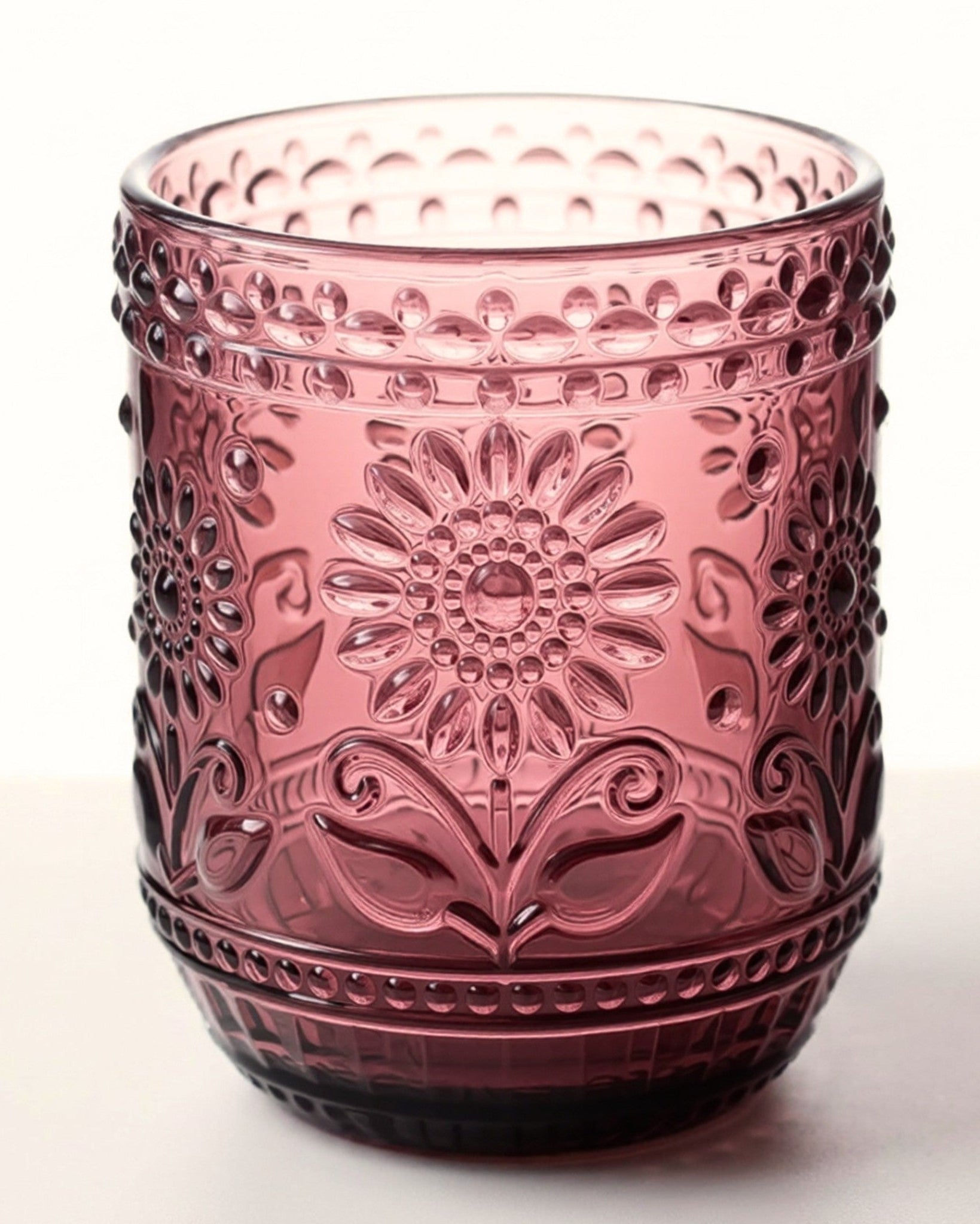 Pink glass tumbler with floral patterns on a white background