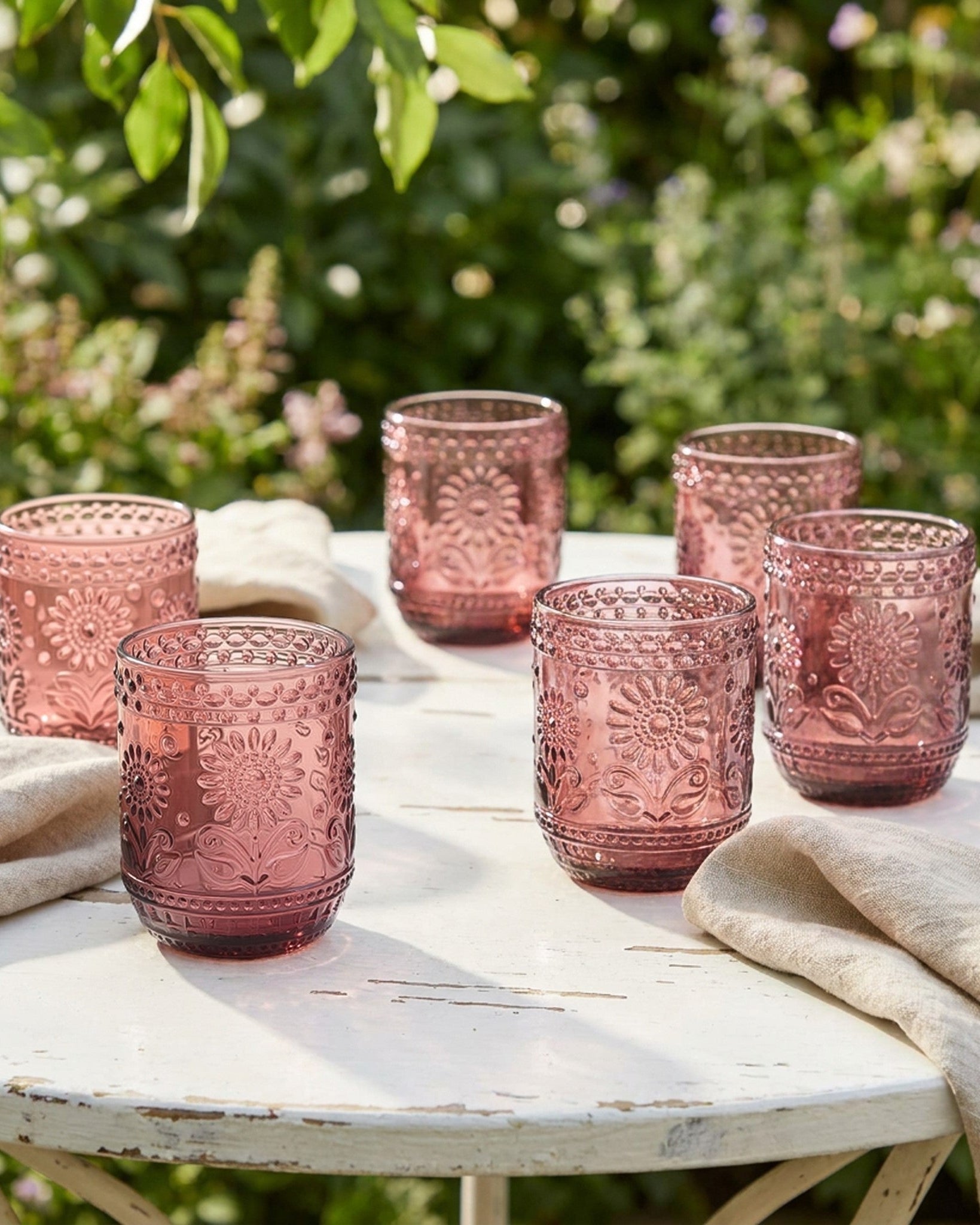 Set of pink textured glasses on a table outdoors with greenery in the background