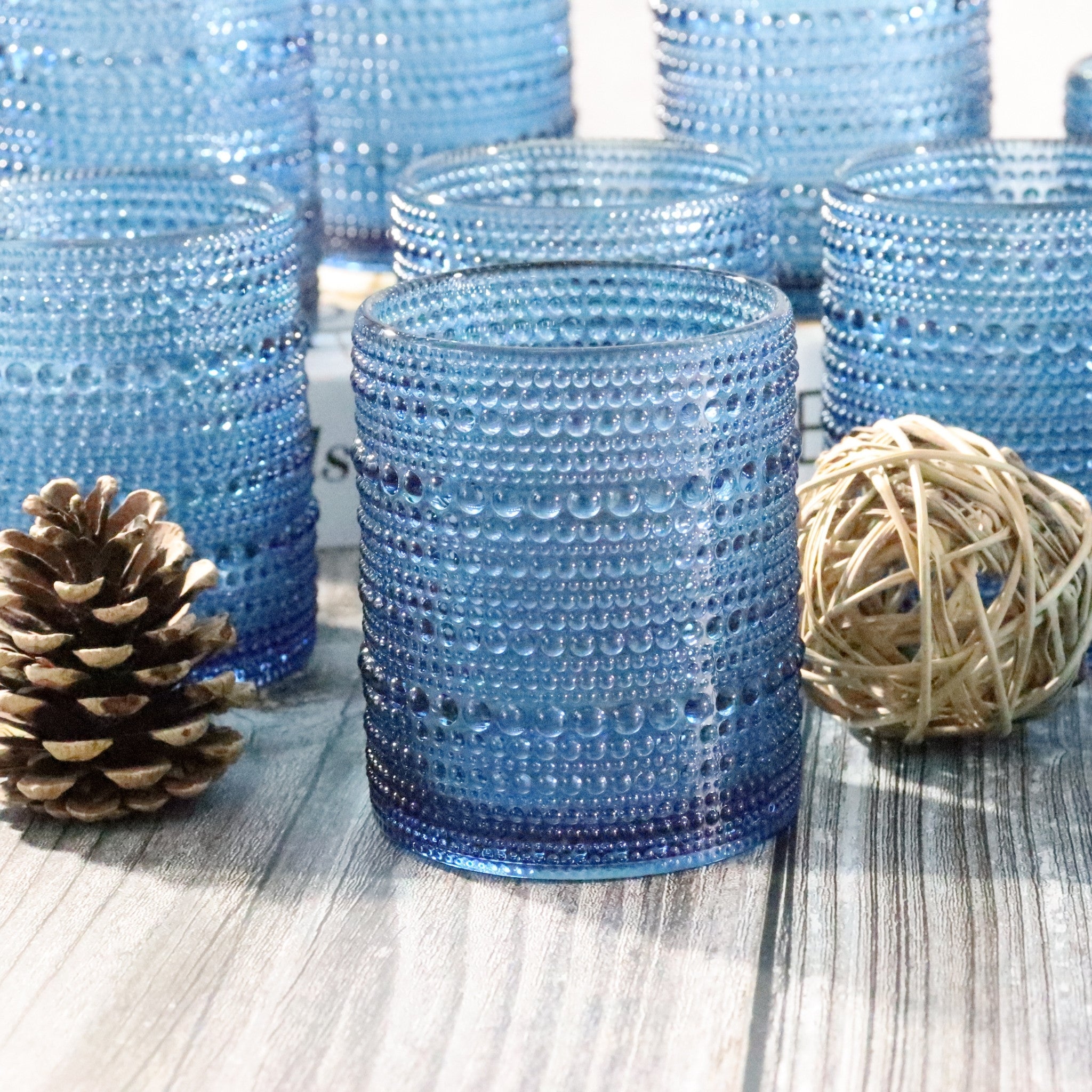 Blue hobnail beaded glass rocks tumblers on a wooden surface with decorative elements.
