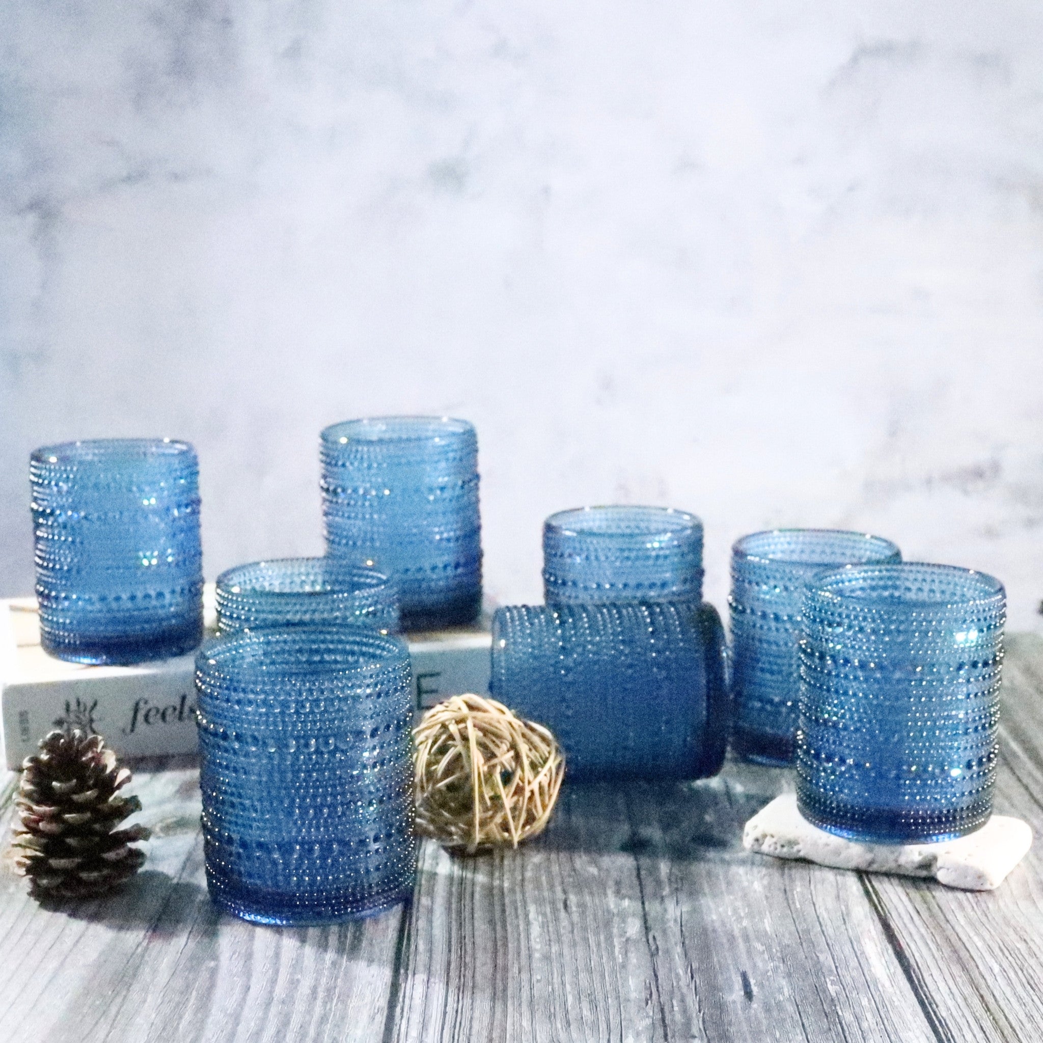 Set of blue textured glass tumblers on a wooden surface with decorative elements.
