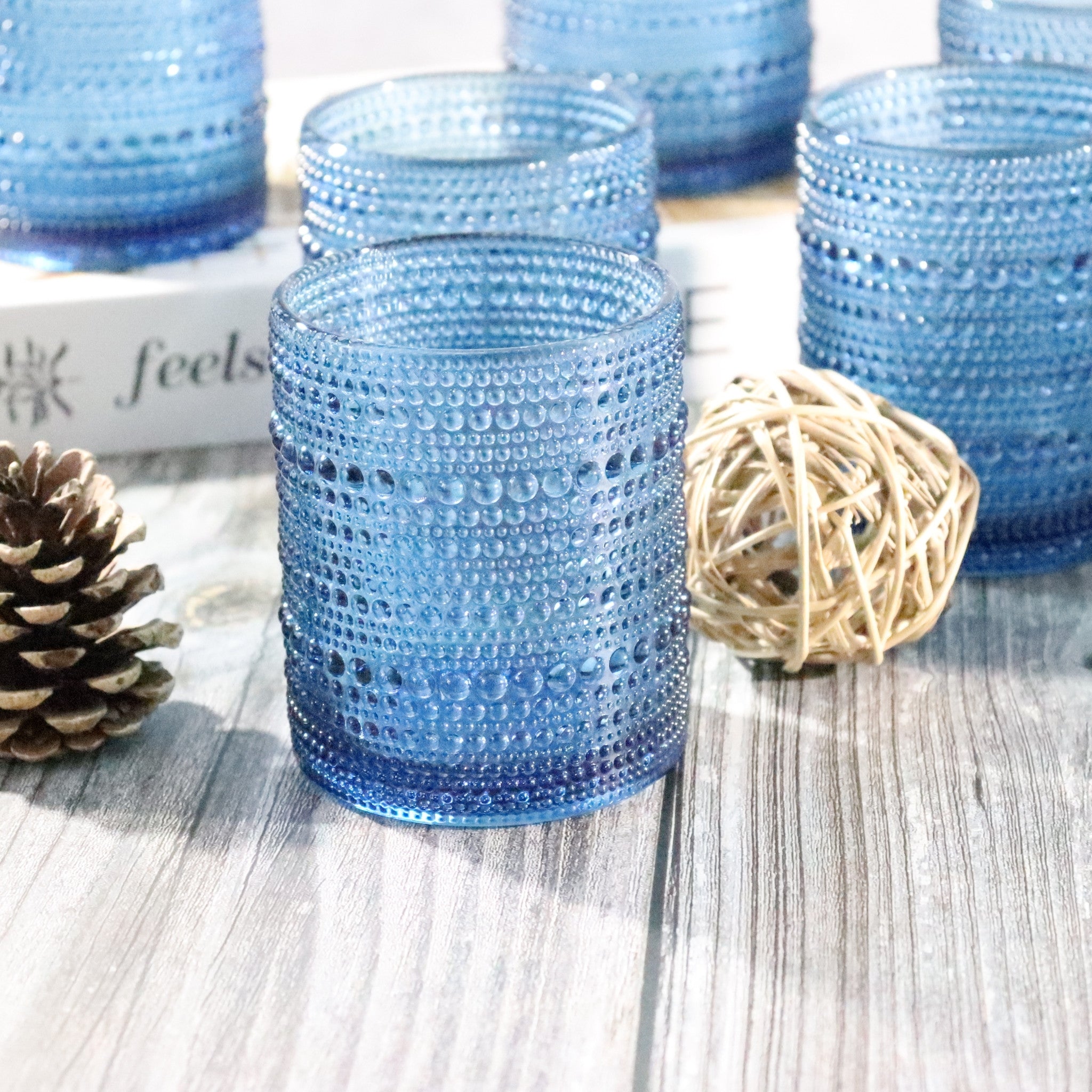 Set of blue Blue hobnail beaded glass rocks tumblers on a light wooden surface with decorative elements.