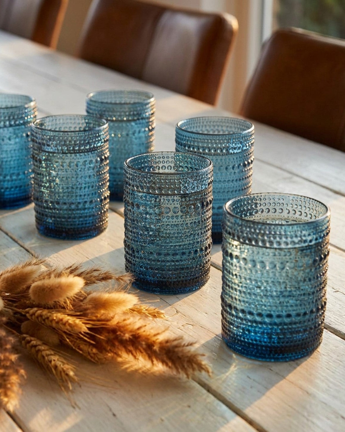 Set of blue textured glass tumblers on a wooden surface with a book in the background.