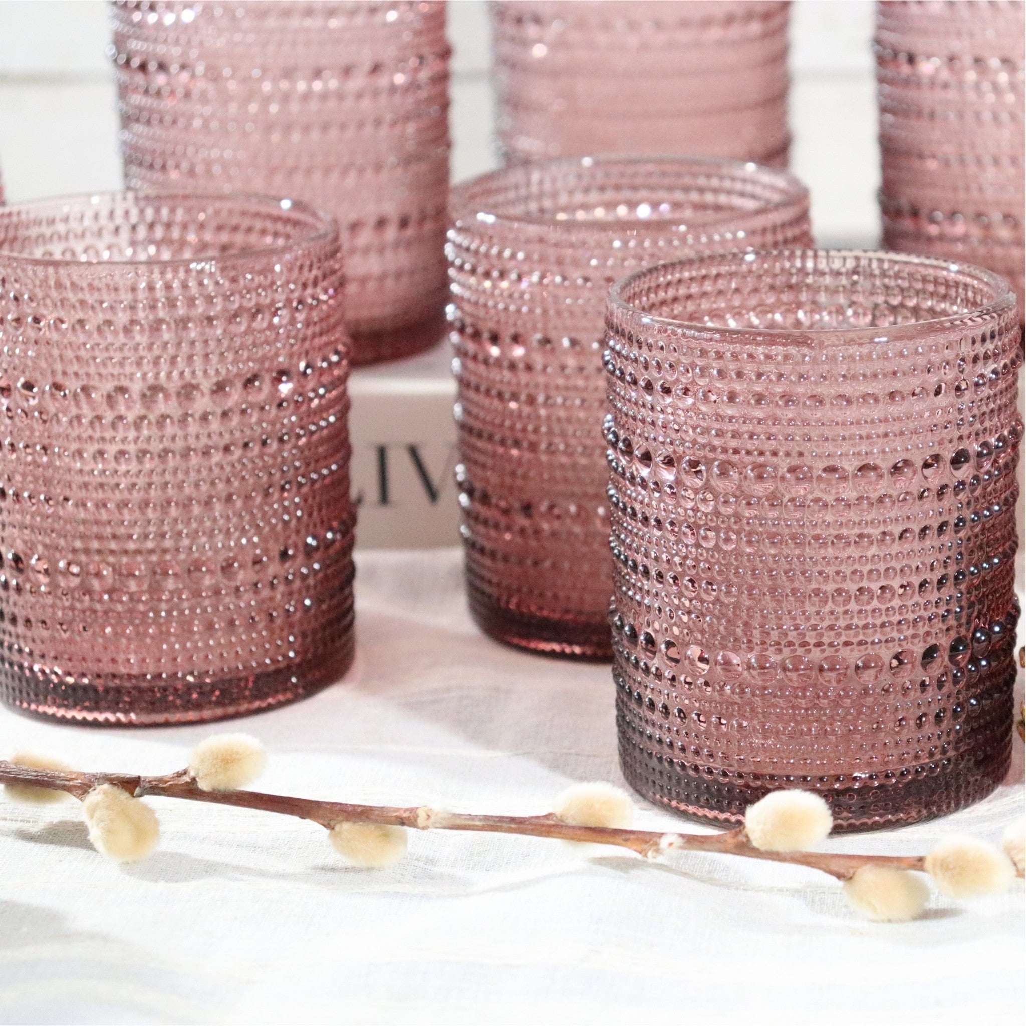 Set of pink beaded glass tumbler on a white surface with a blurred background.