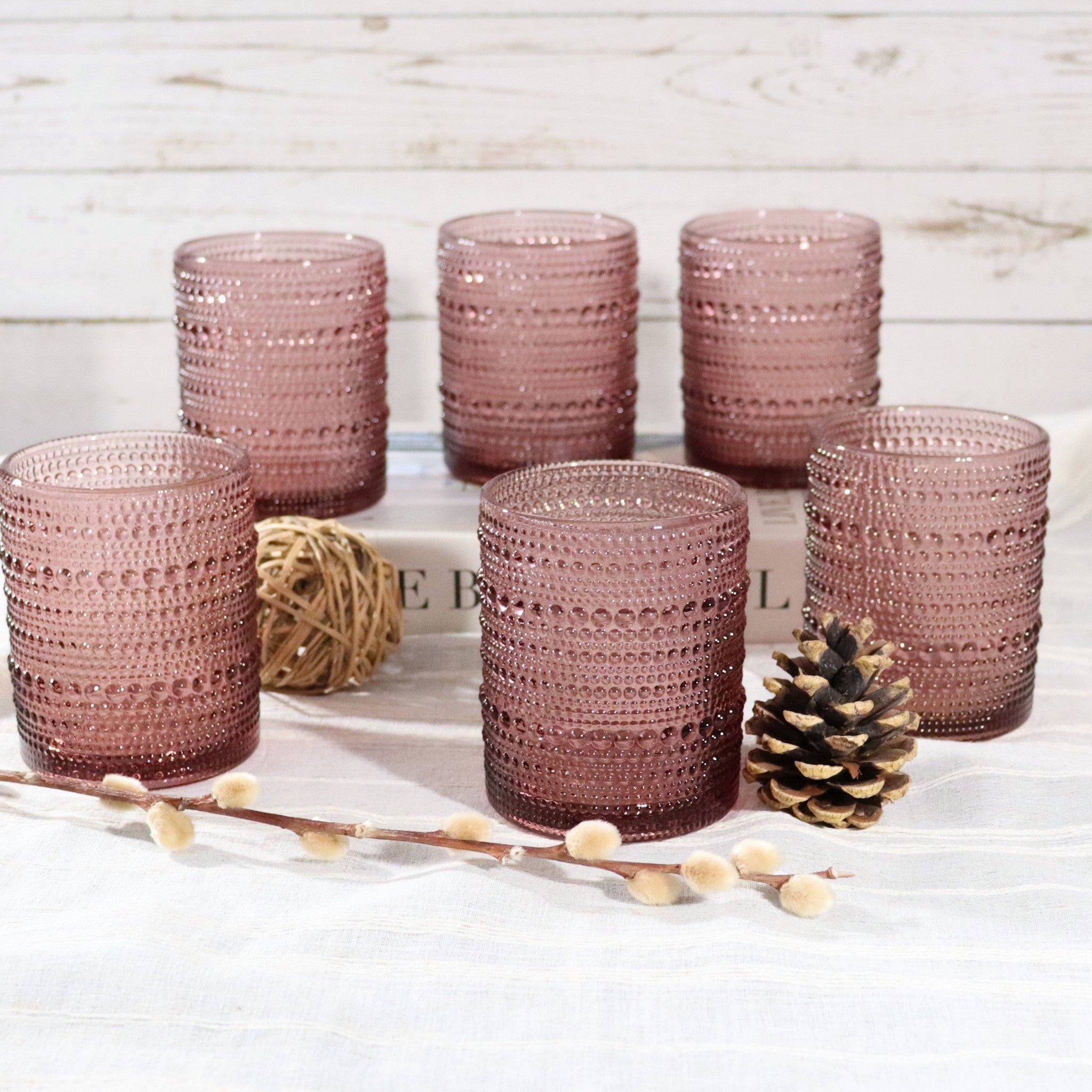 Set of six pink textured glass tumblers on a light wooden surface with decorative elements.