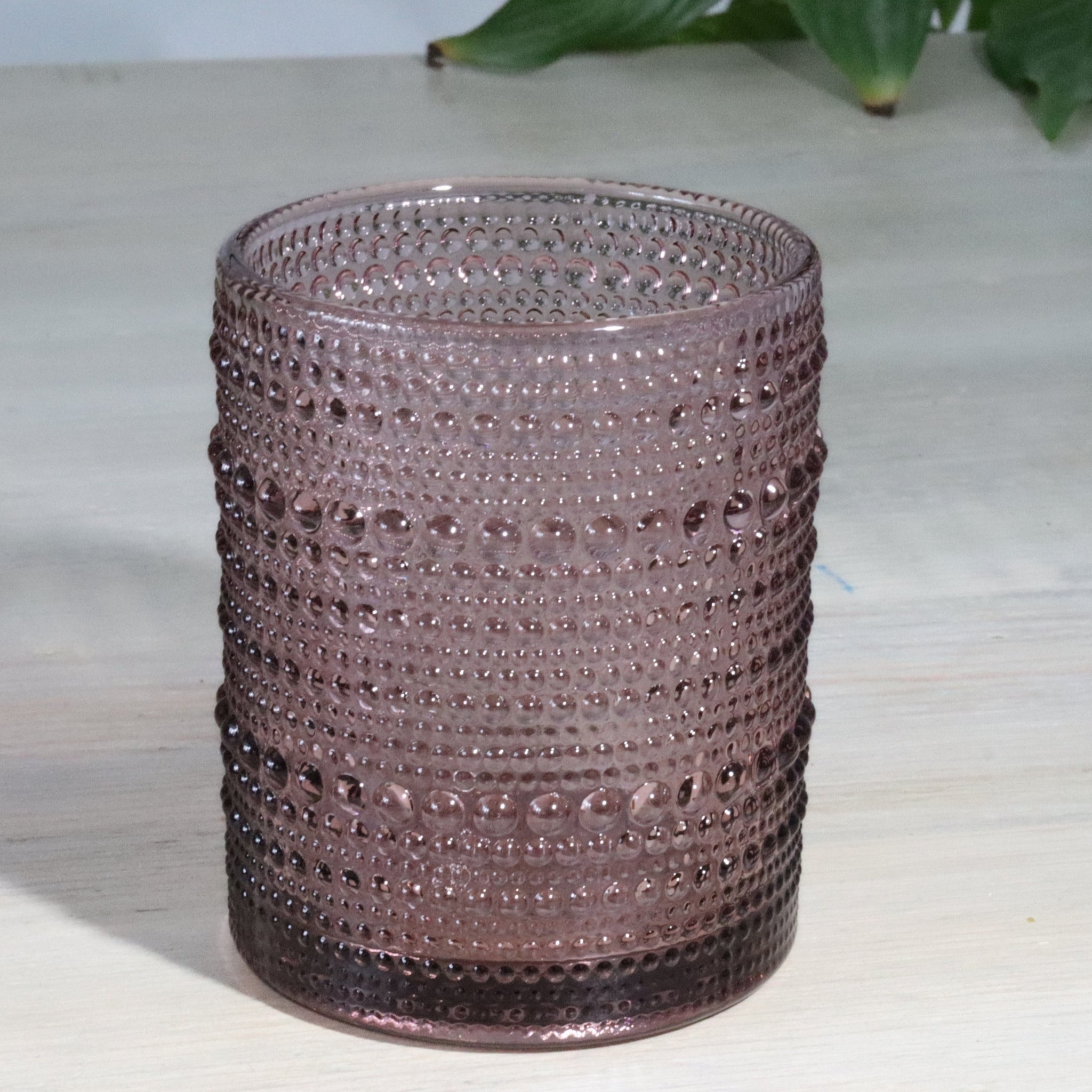 one pink hobnail glass tumblers on a white surface with greenery in the background