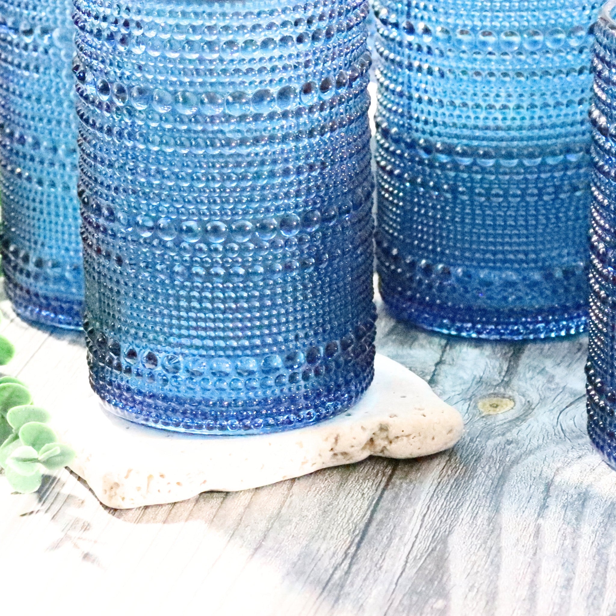 Blue hobnail jupiter bead hi-ball tumblers on a wooden surface with a shell and greenery