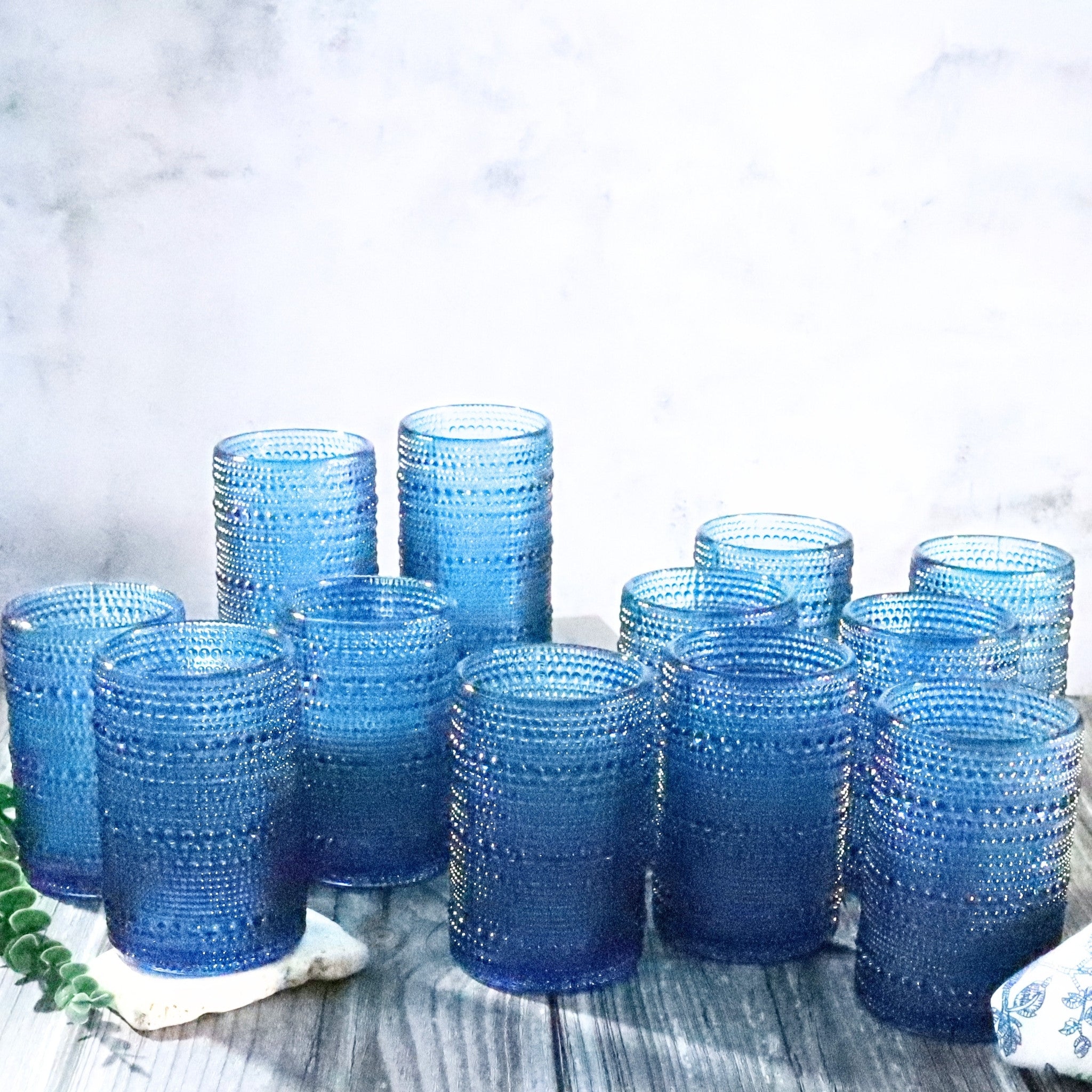 Set of blue textured glass tumblers on a wooden surface with a light background