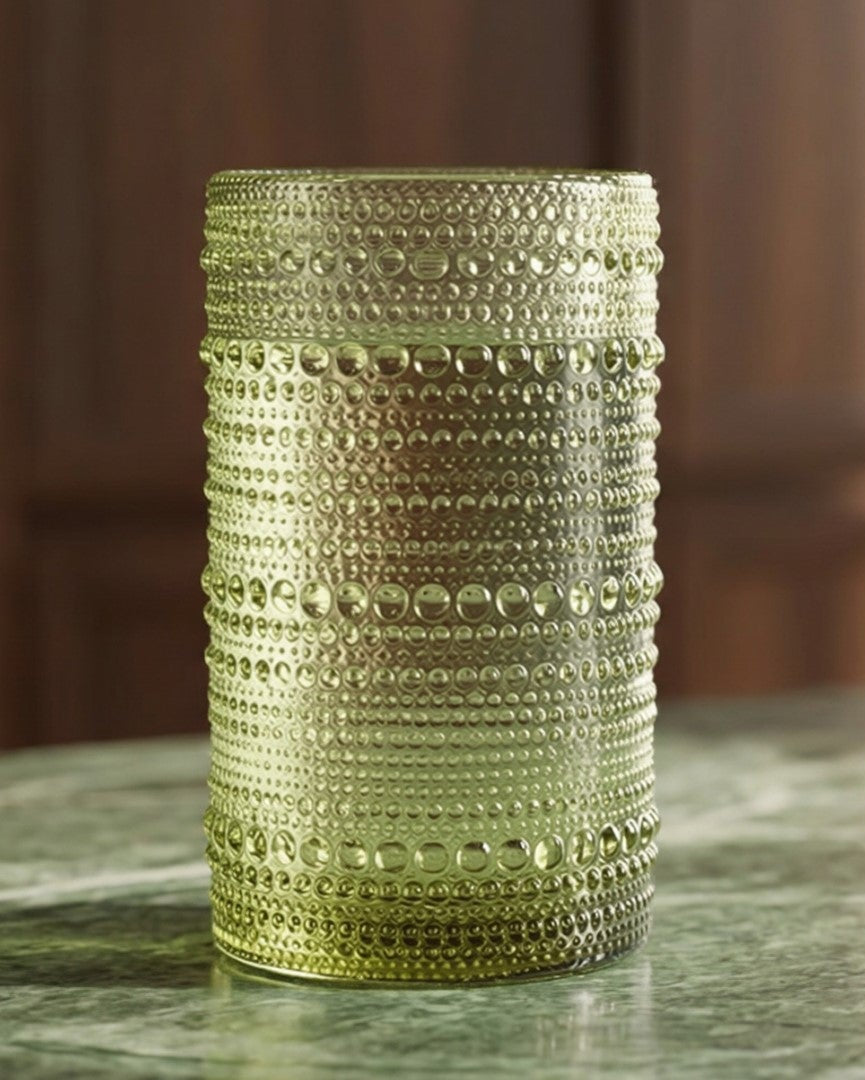 Green textured glass candle holders on a wooden surface with a book and flower.