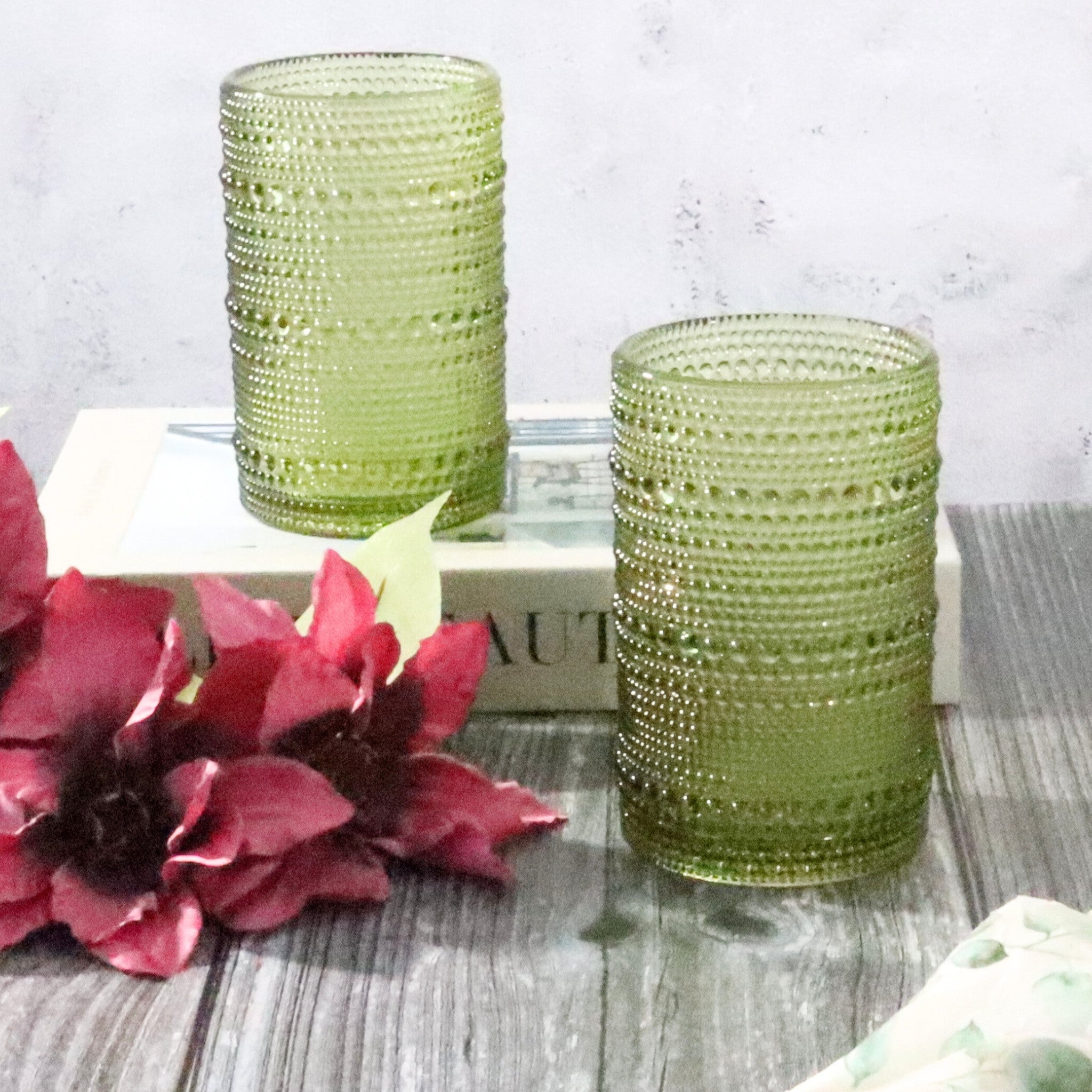 Two green textured hobnail bead glass on a wooden surface with pink flowers.