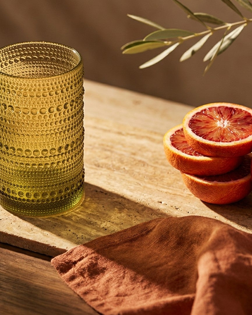 Set of green textured glass tumblers on a wooden surface with flowers and a box in the background.
