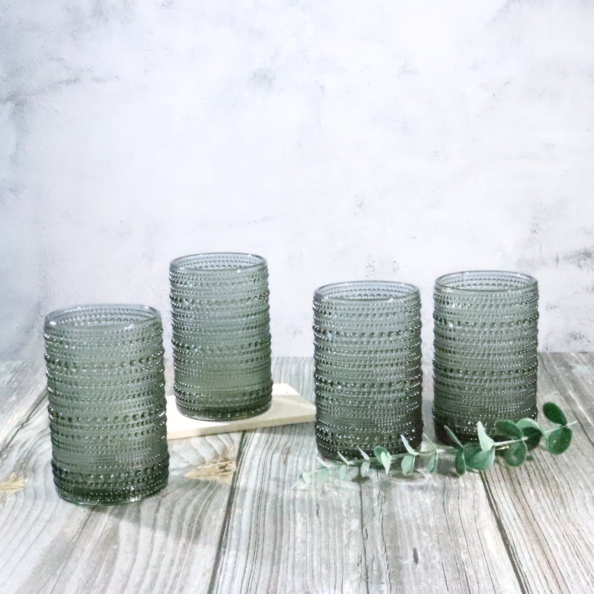 Set of four hobnail jupiter bead grey glass tumblers on a wooden surface with a white marble background