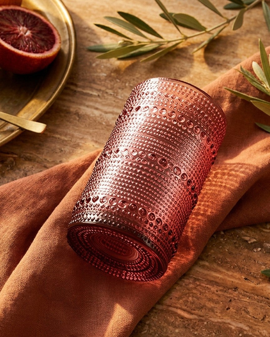 Pink textured glass on a wooden surface with olives and blood oranges.