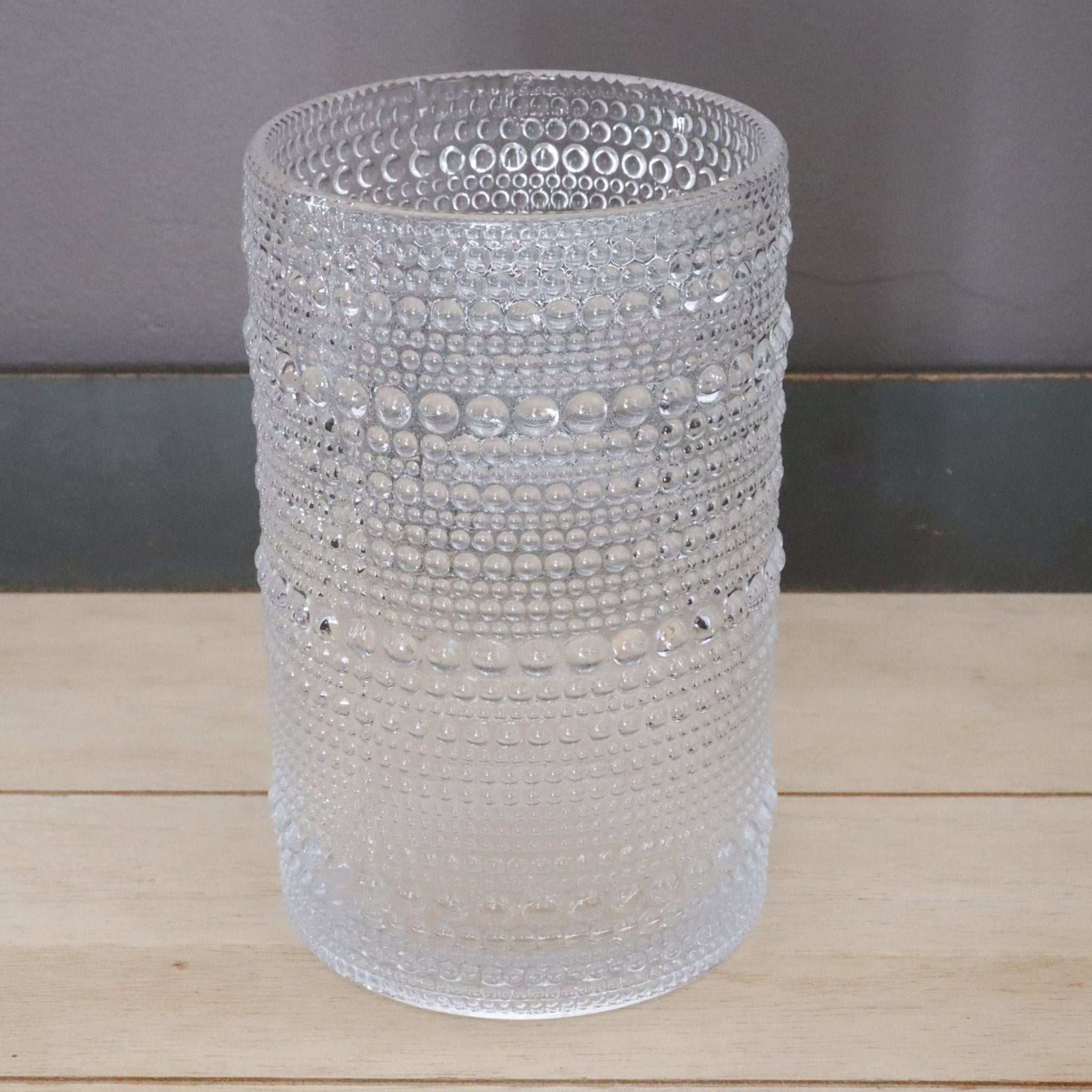 Clear hobnail hi-ball tumbler on a wooden surface with a gray background