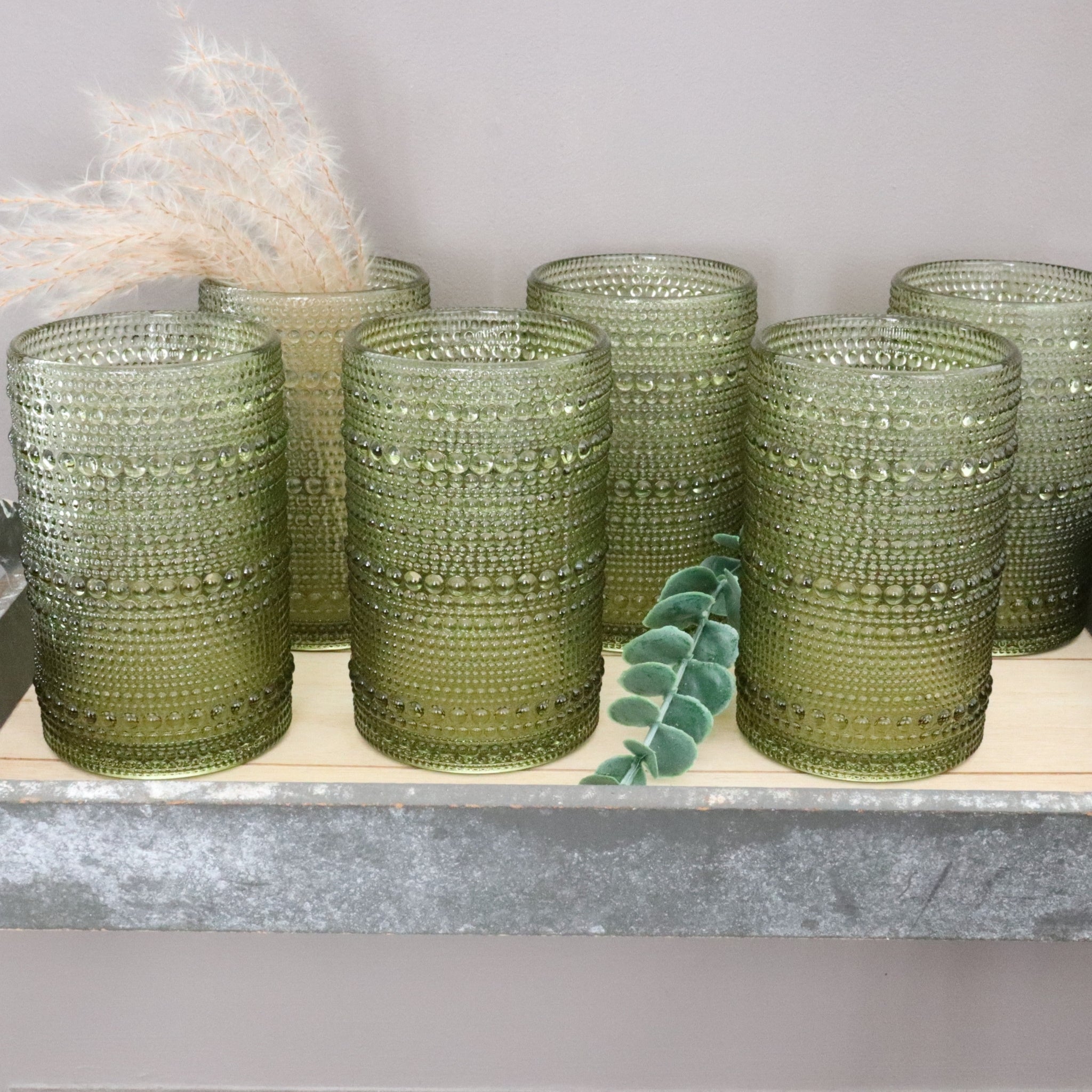 Set of green hobnail glass tumblers on a light surface with a neutral background
