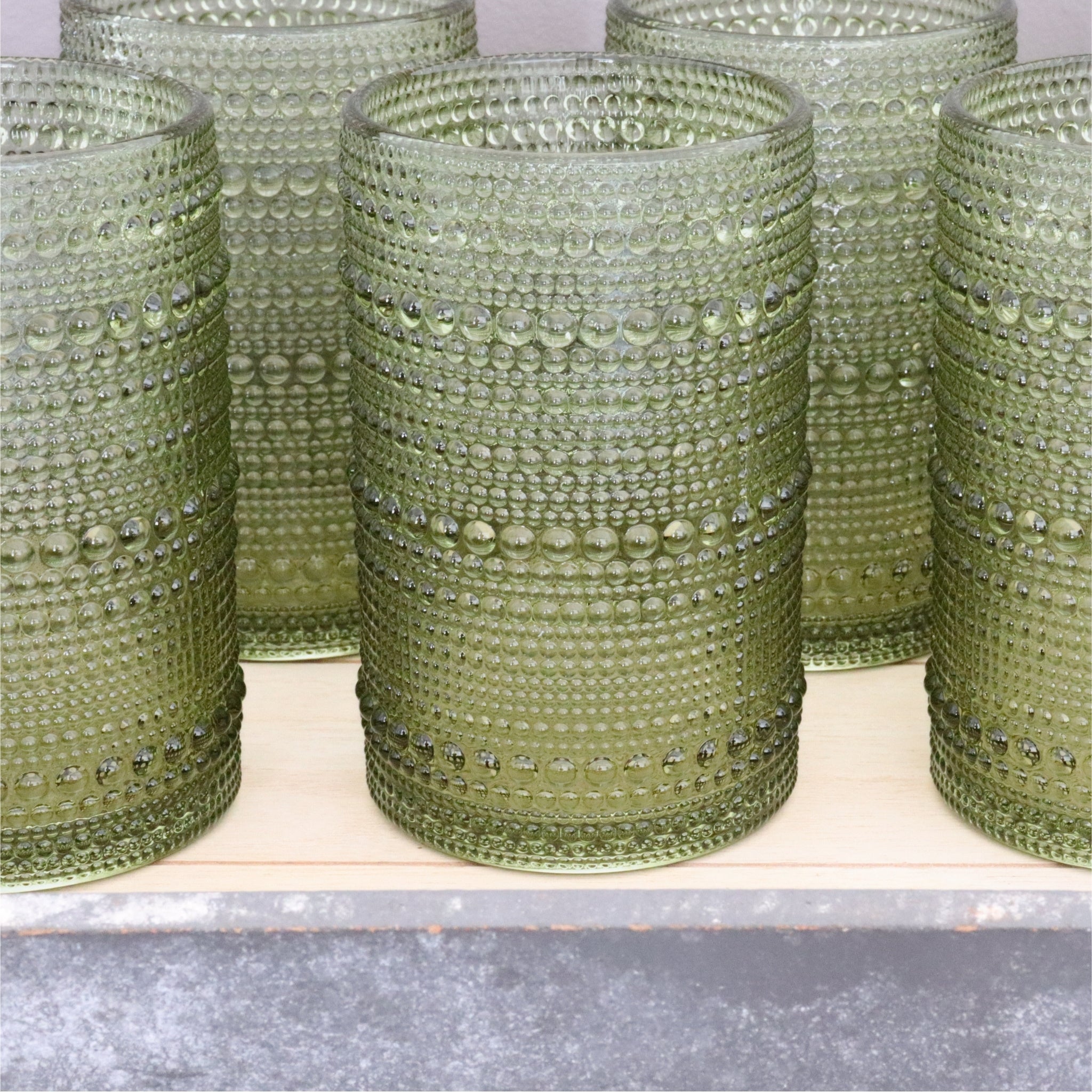 Set of green hobnail glasses on a wooden surface.