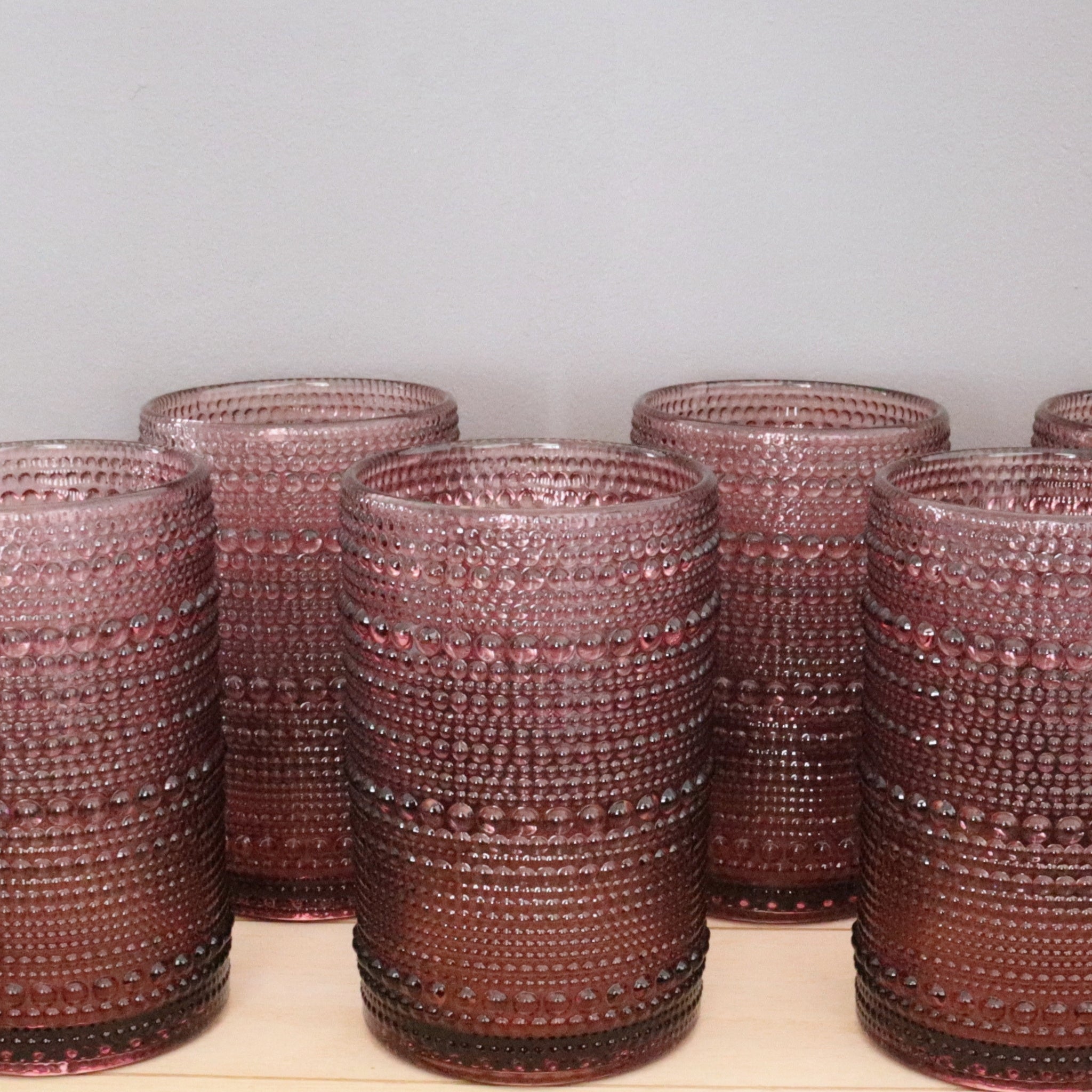 Set of hobnail purple glass tumblers with textured surface on a light wooden surface.