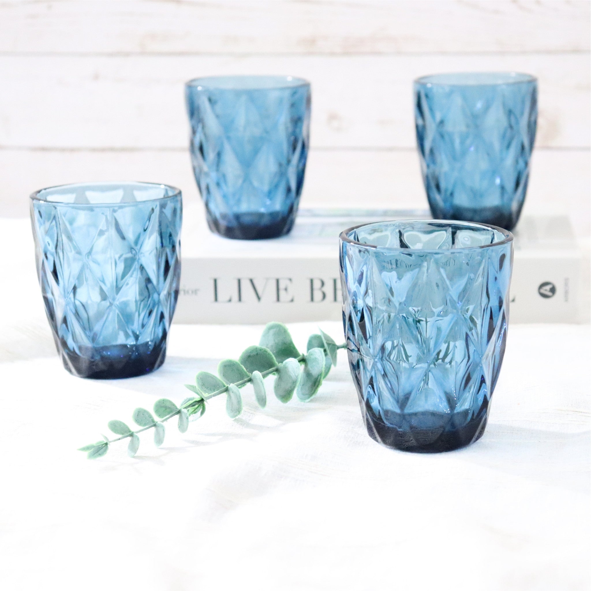 Set of four blue textured glass tumblers on a white surface with a plant leaf.