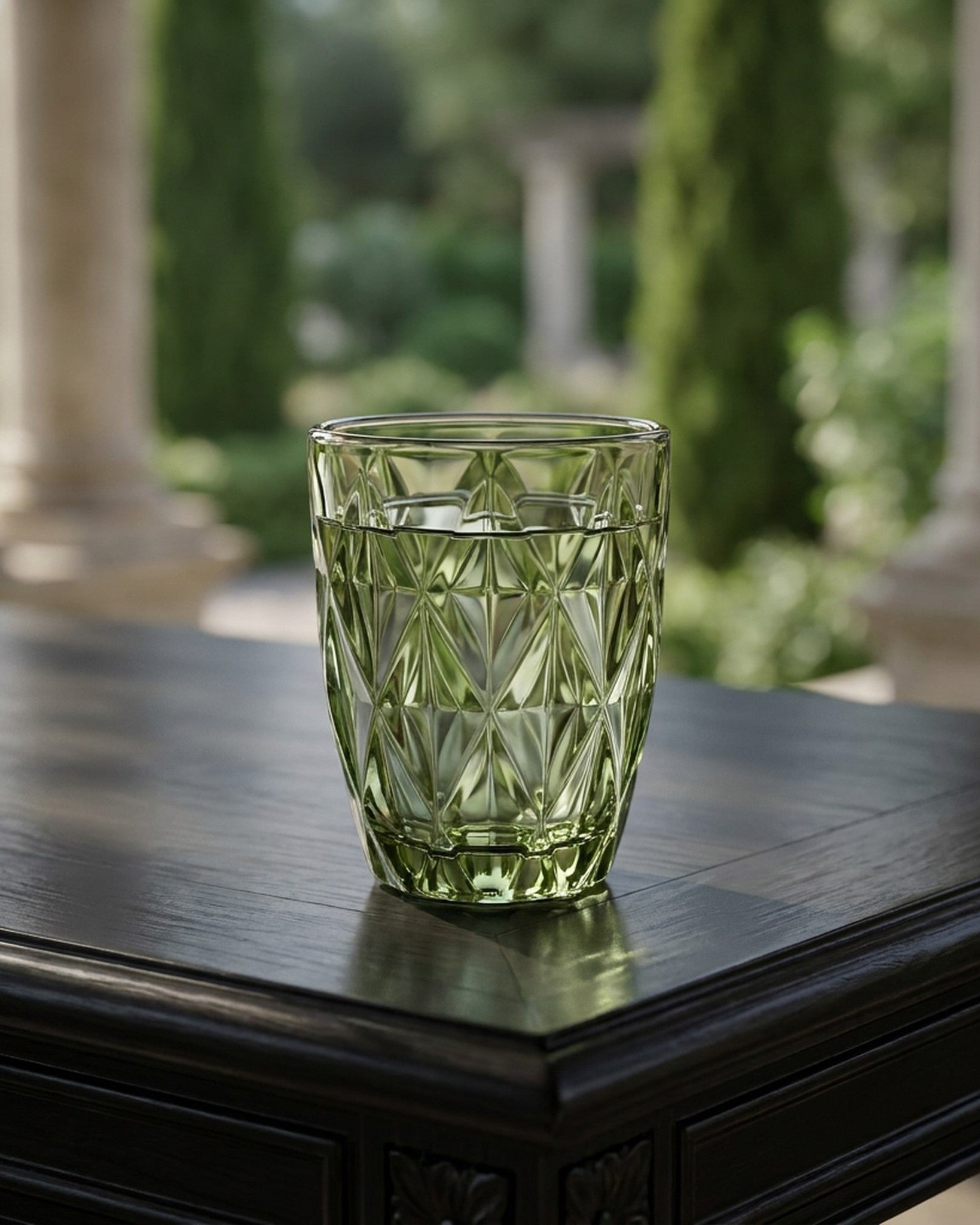 Green glass tumbler on a dark wooden surface with a blurred garden background