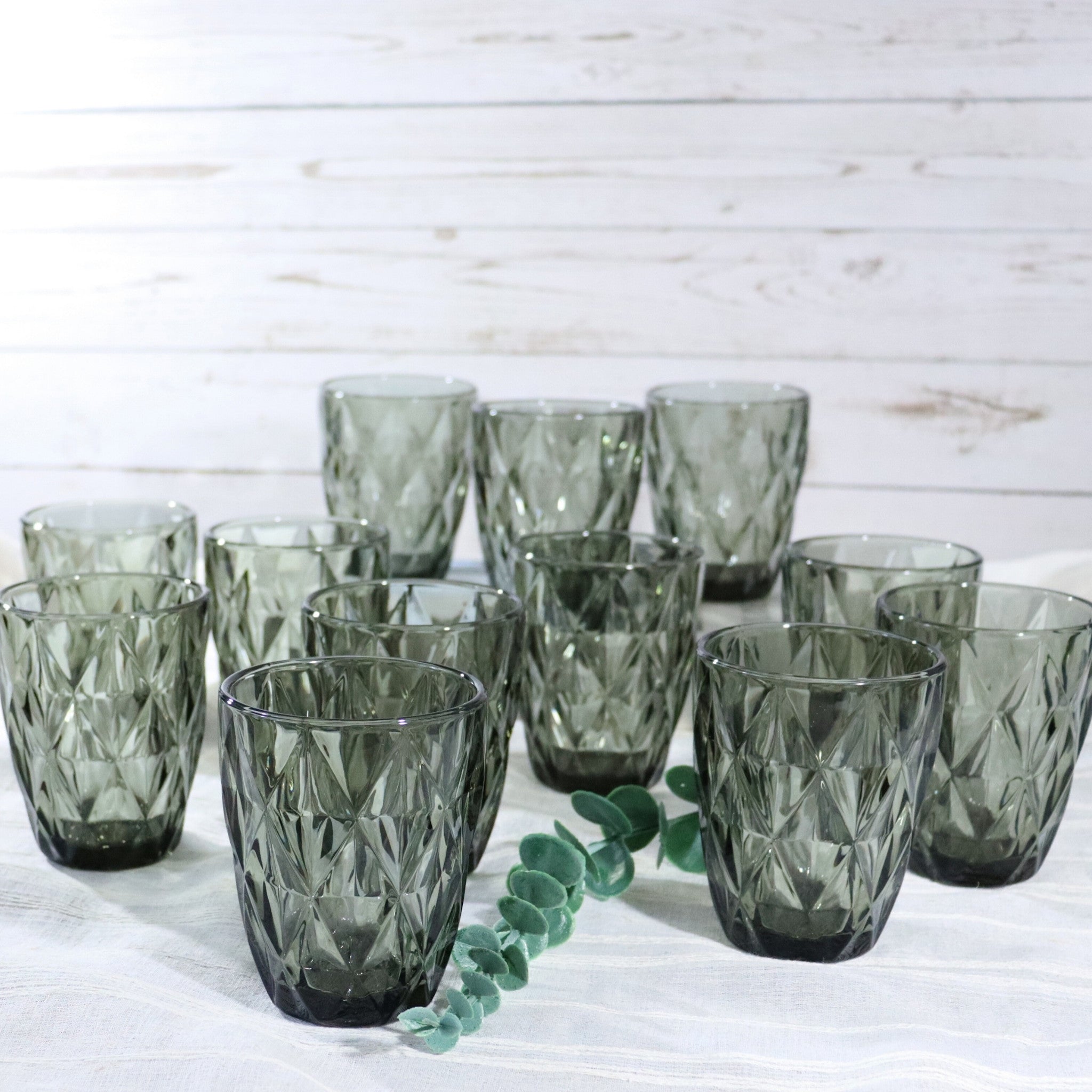 Set of green glass tumblers on a white wooden surface with a light wooden background