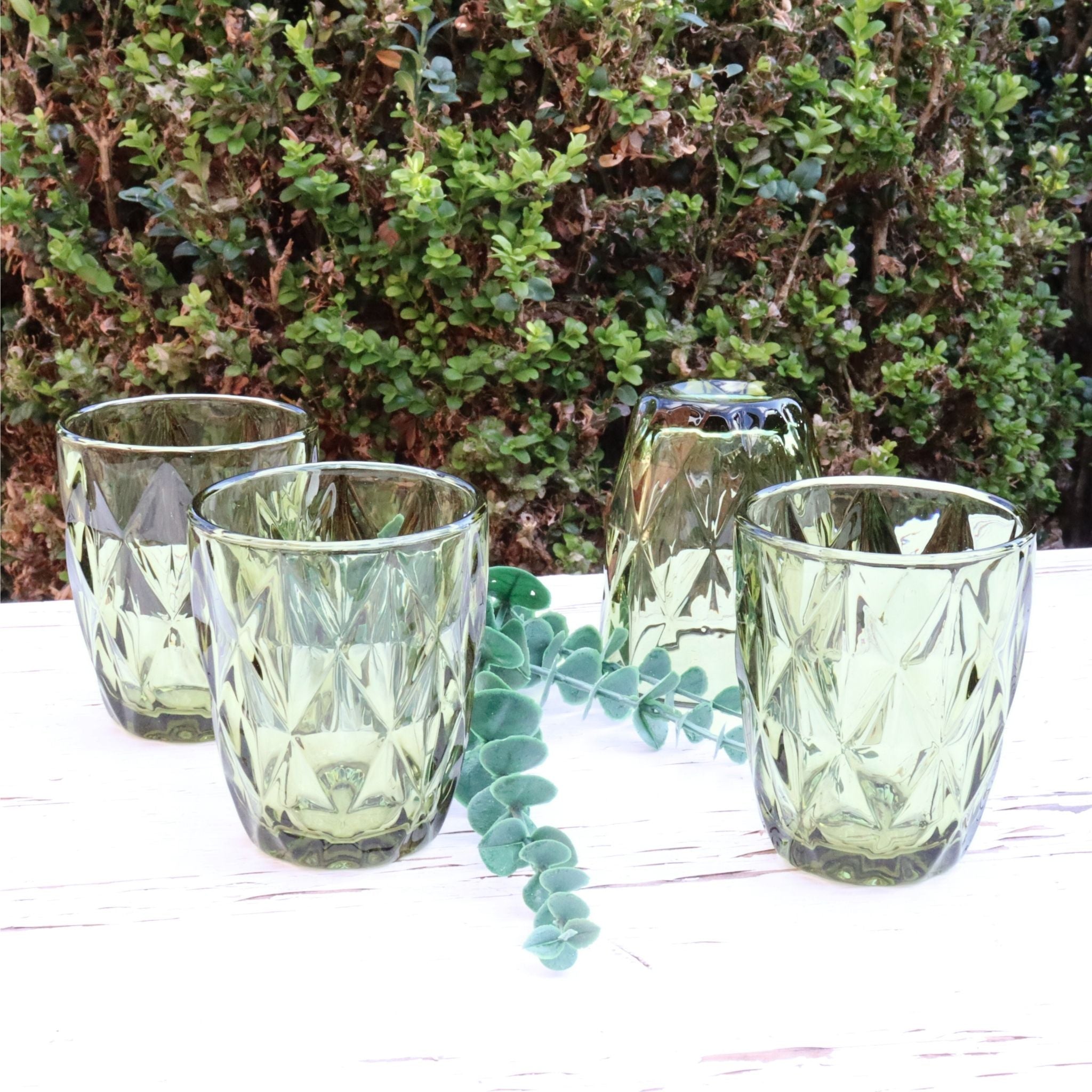 Set of green glass tumblers on a white surface with a blurred natural background