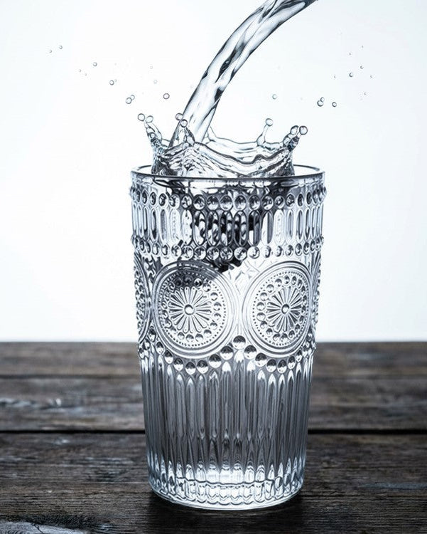 Set of four clear glass tumblers on a wooden surface with a neutral background