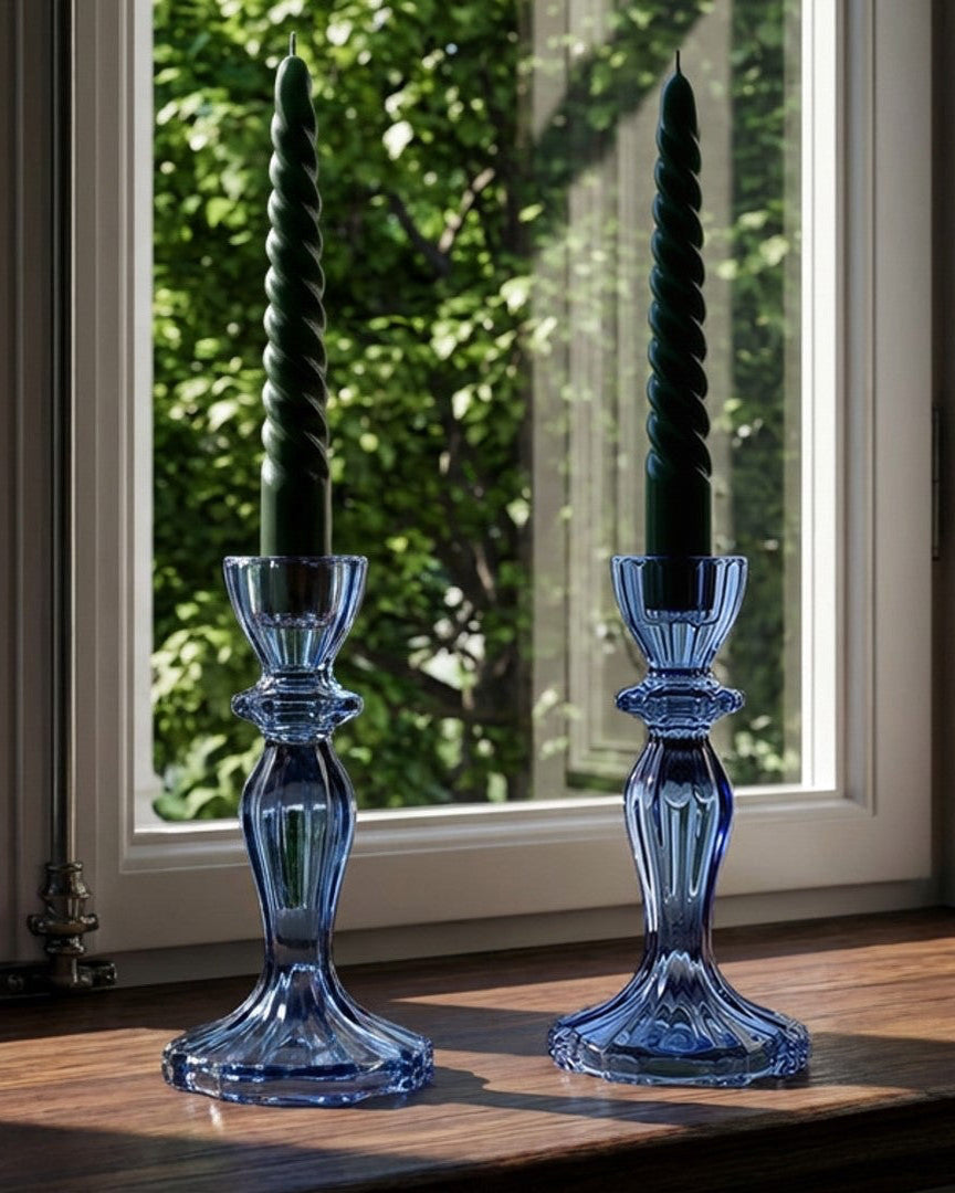 Two blue glass candle holders with black candles on a wooden surface in front of a window.