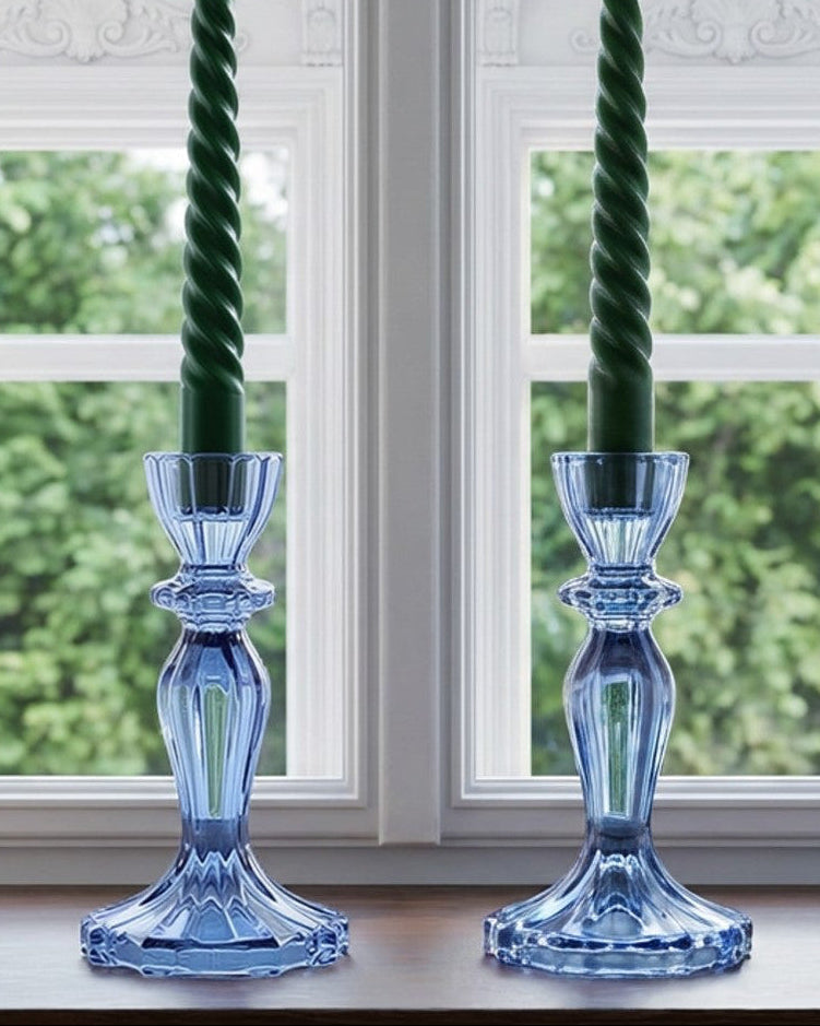 Two blue glass candle holders with green candles on a windowsill.
