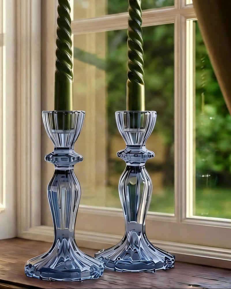 Two blue glass candlesticks with green candles on a windowsill.