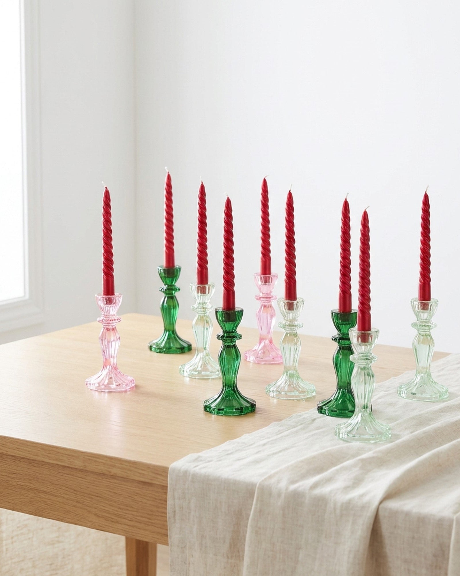 Two red spiral candles in green candlesticks on a wooden surface with white flowers.