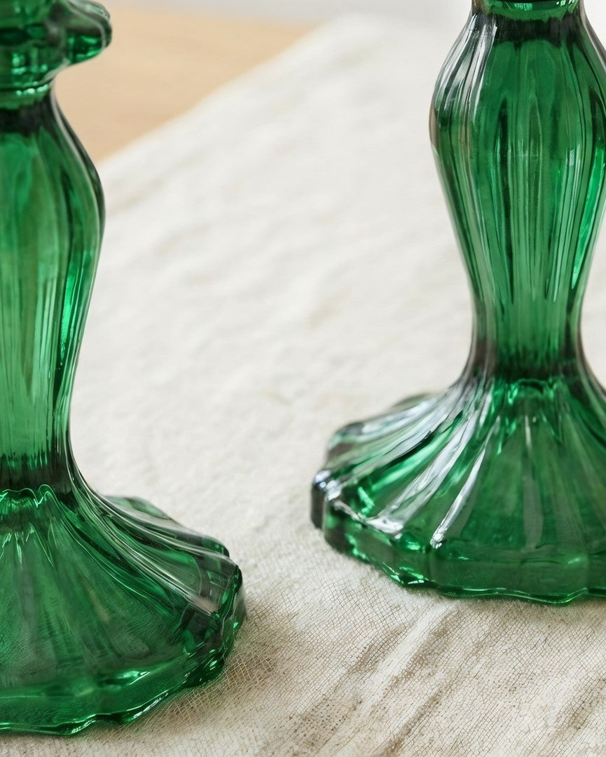 Two green ribbed glass candlestick holders with flared bases, displayed on a beige fabric surface.